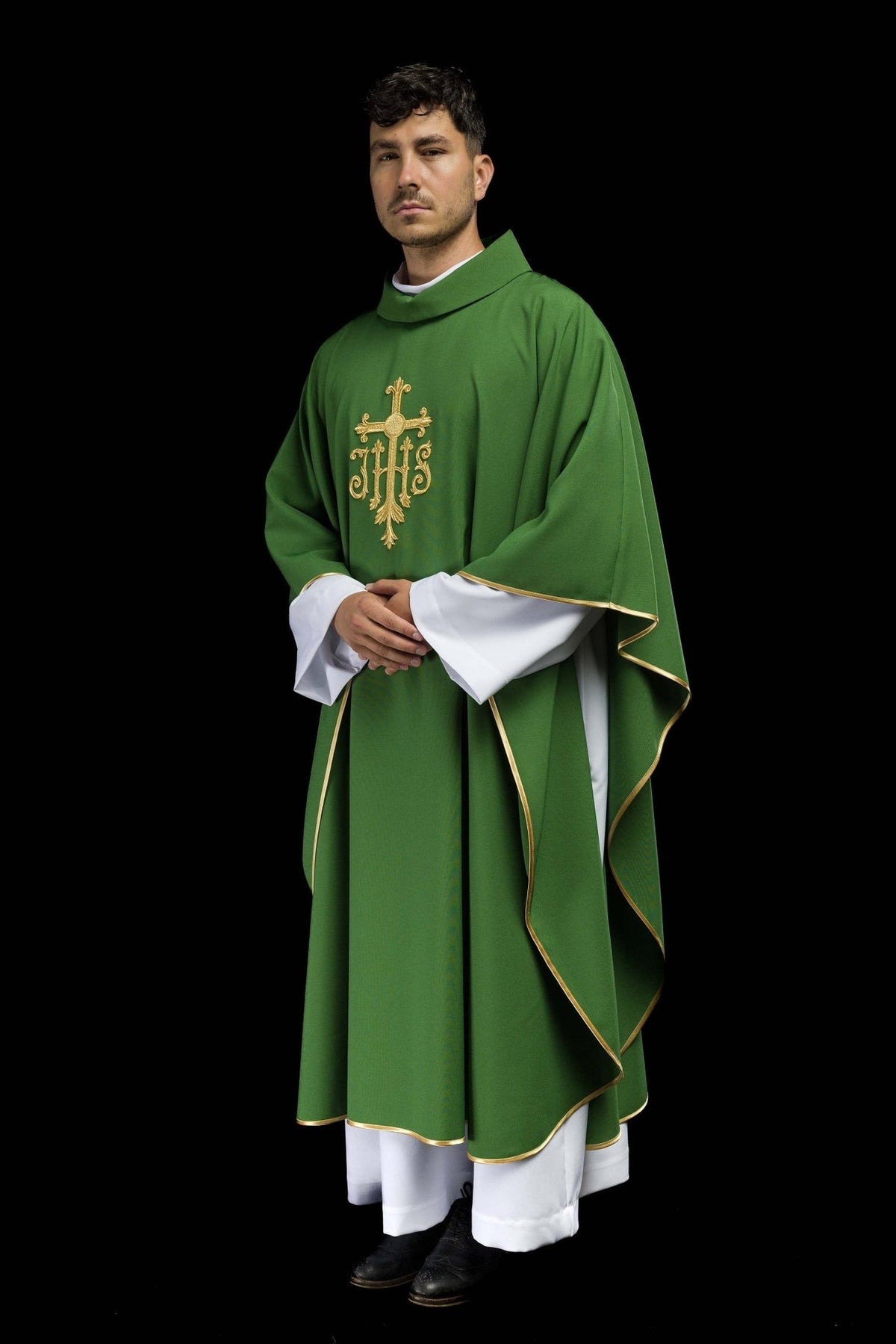 Green chasuble worn from the side, showing its flowing shape, gold trim and JHS embroidery