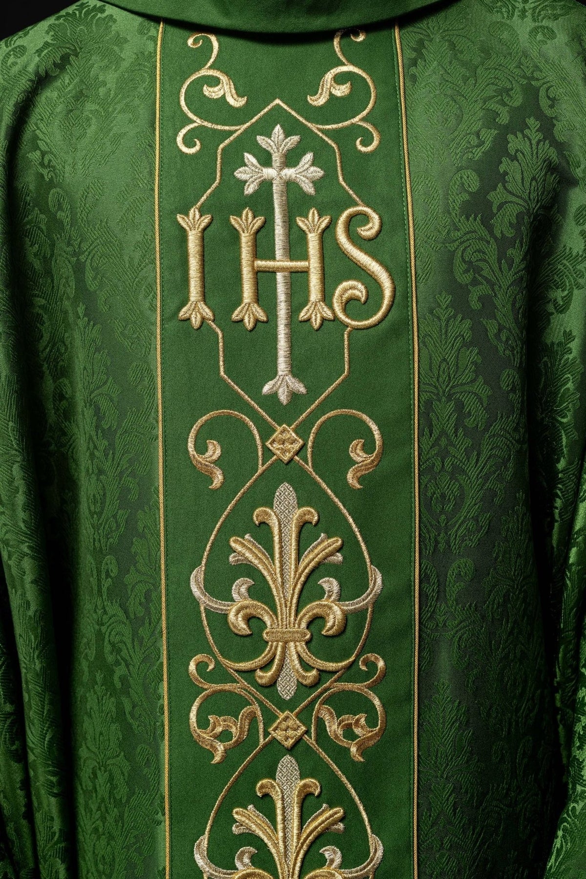 Green chasuble close-up showing IHS embroidery and floral-patterned fabric