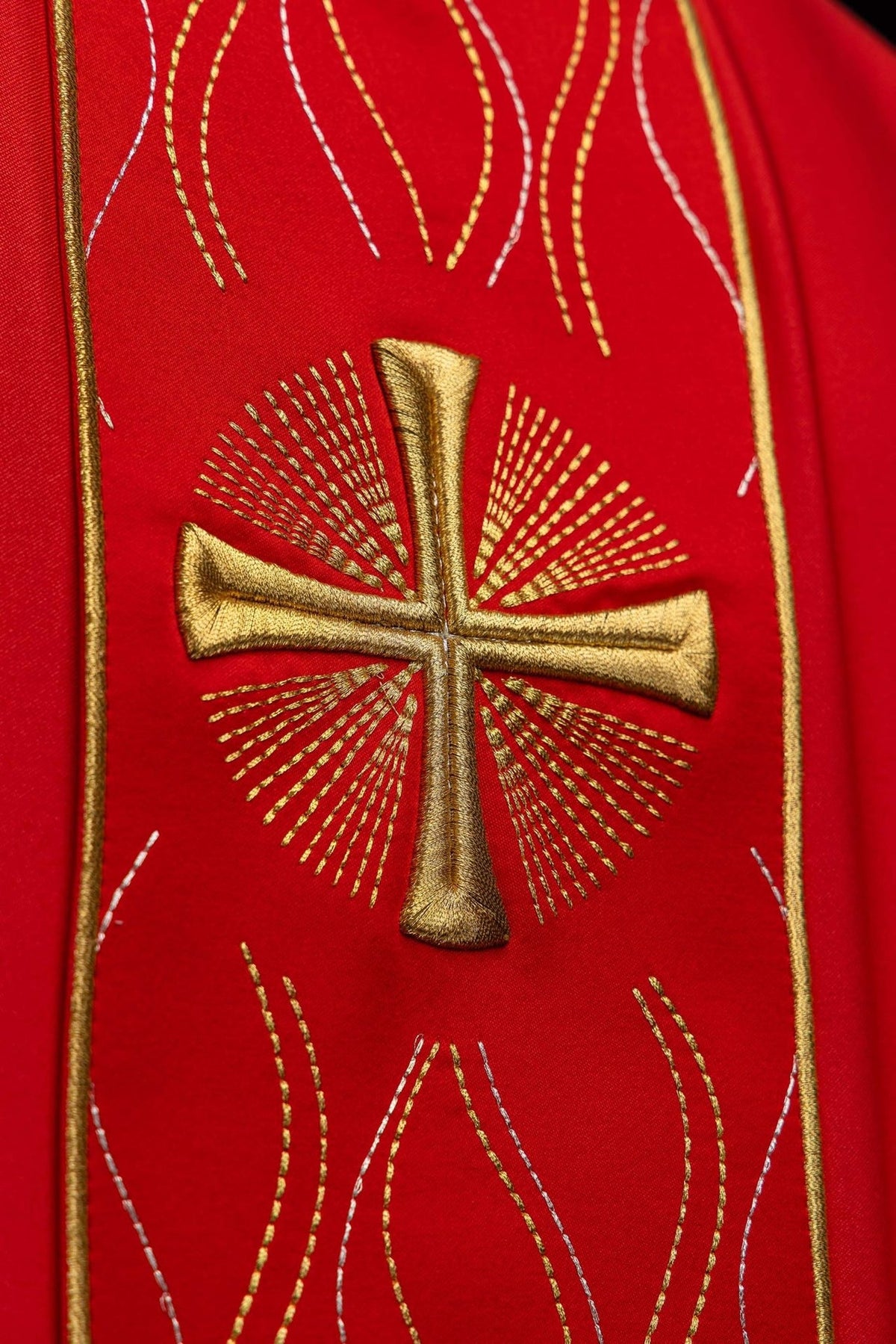 Red chasuble detail showing embroidered gold cross with radiating lines