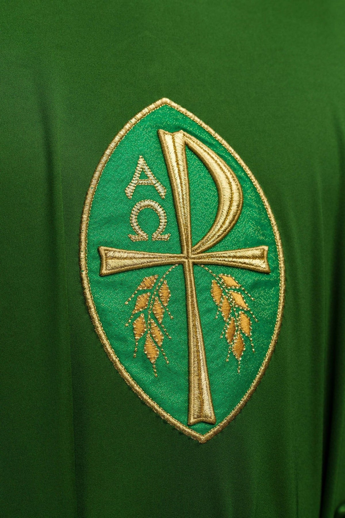Green chasuble close-up showing gold embroidered cross, Alpha and Omega, and wheat motifs