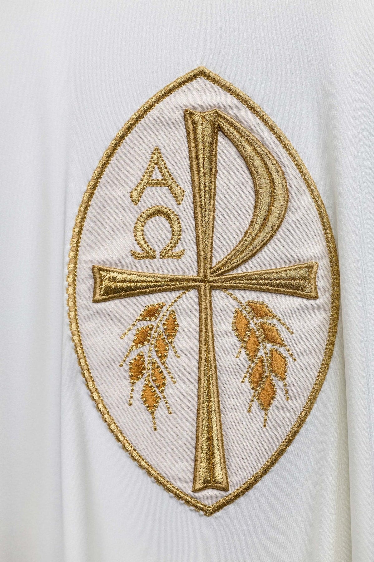 Ecru chasuble close-up showing gold embroidered cross with Alpha and Omega symbols
