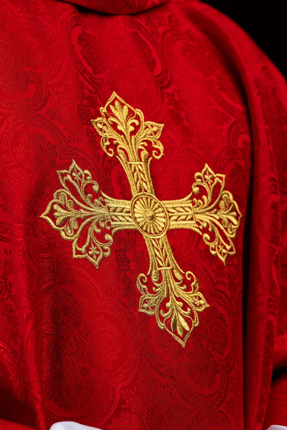 Red chasuble close-up showing gold cross embroidery on jacquard fabric