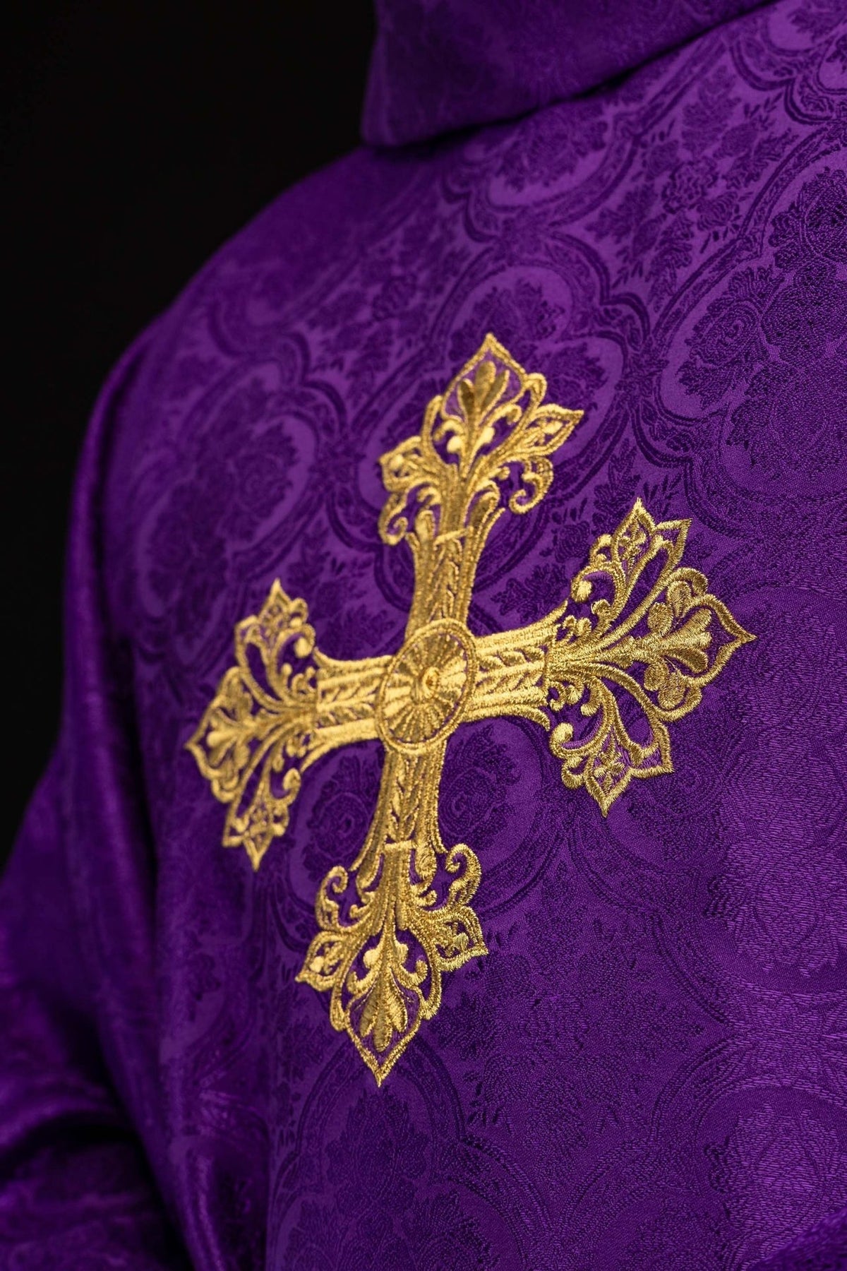Purple chasuble close-up of ornate gold cross embroidery on patterned fabric