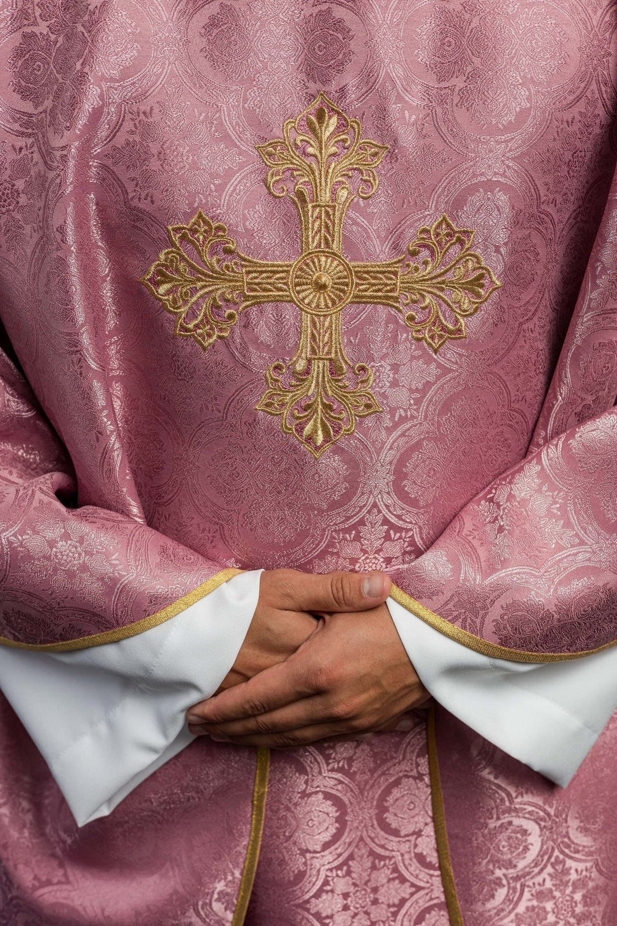 Rose chasuble close-up showing ornate gold embroidered cross on patterned fabric
