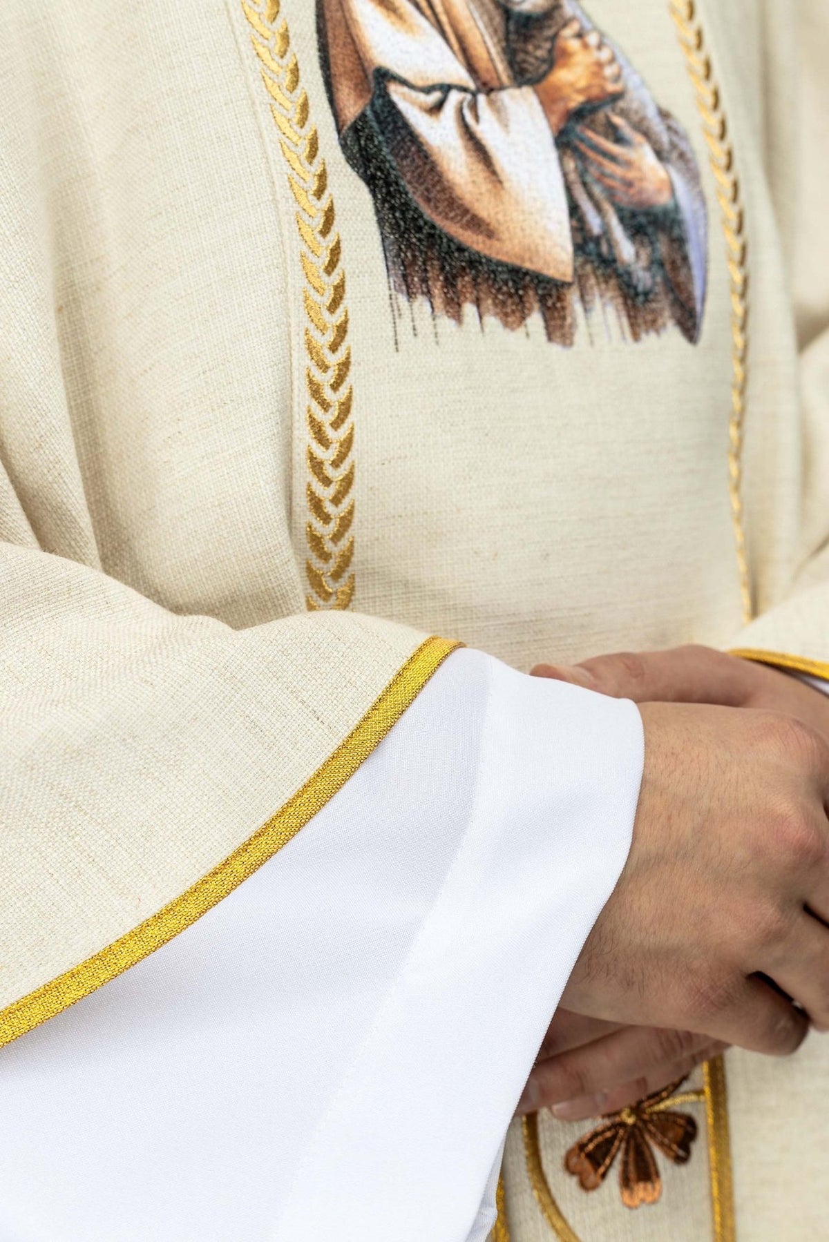 Ecru chasuble detail showing gold braided orphrey trim and Good Shepherd image