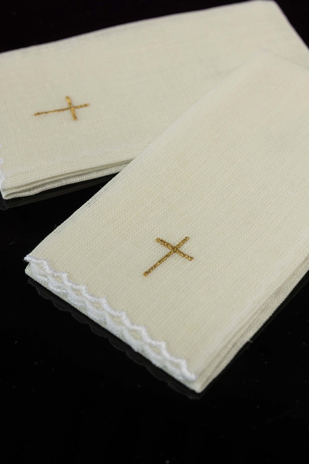 Linen purificators close-up showing gold cross embroidery and white scalloped edges