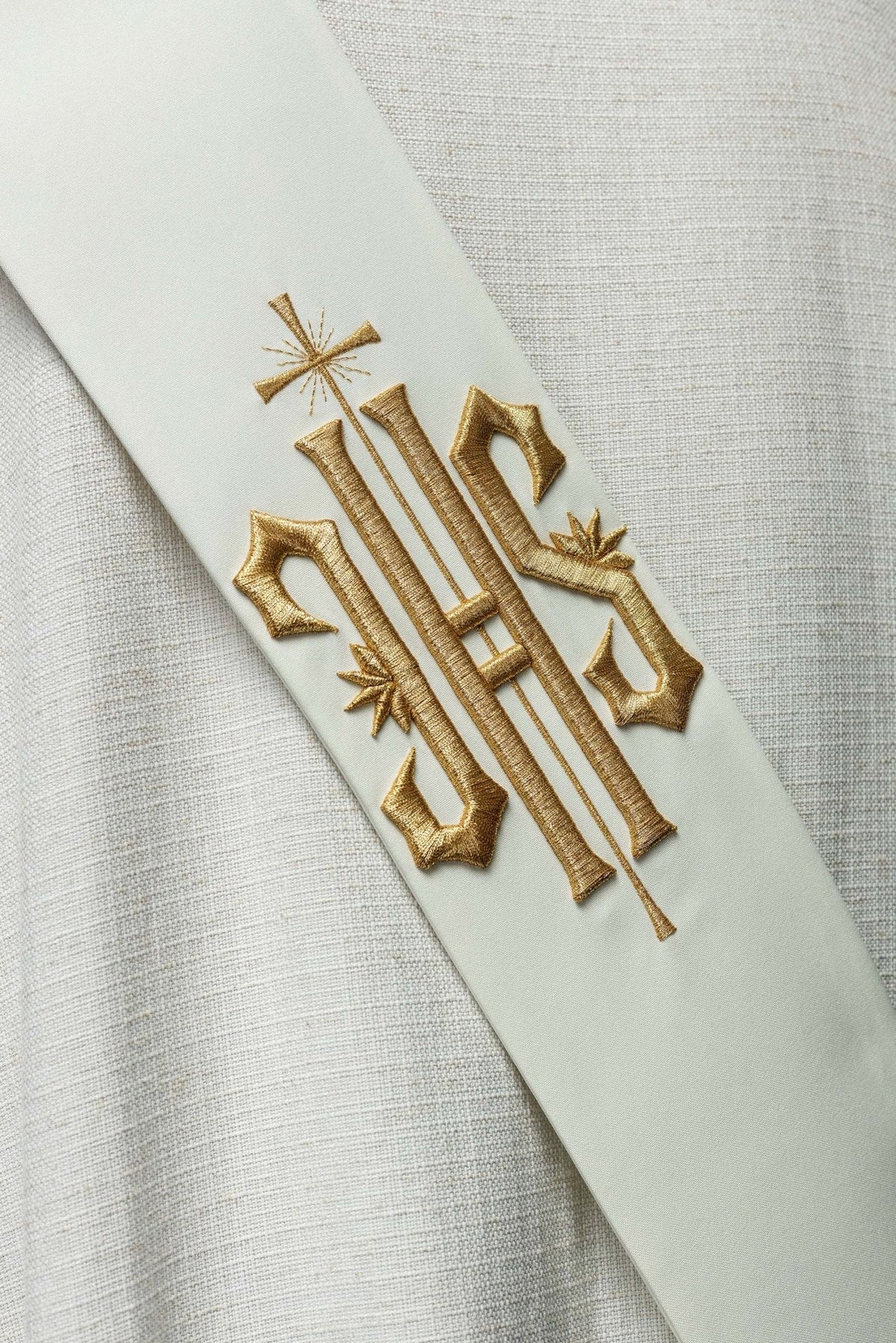 White deacon stole worn from the back with gold IHS embroidery visible