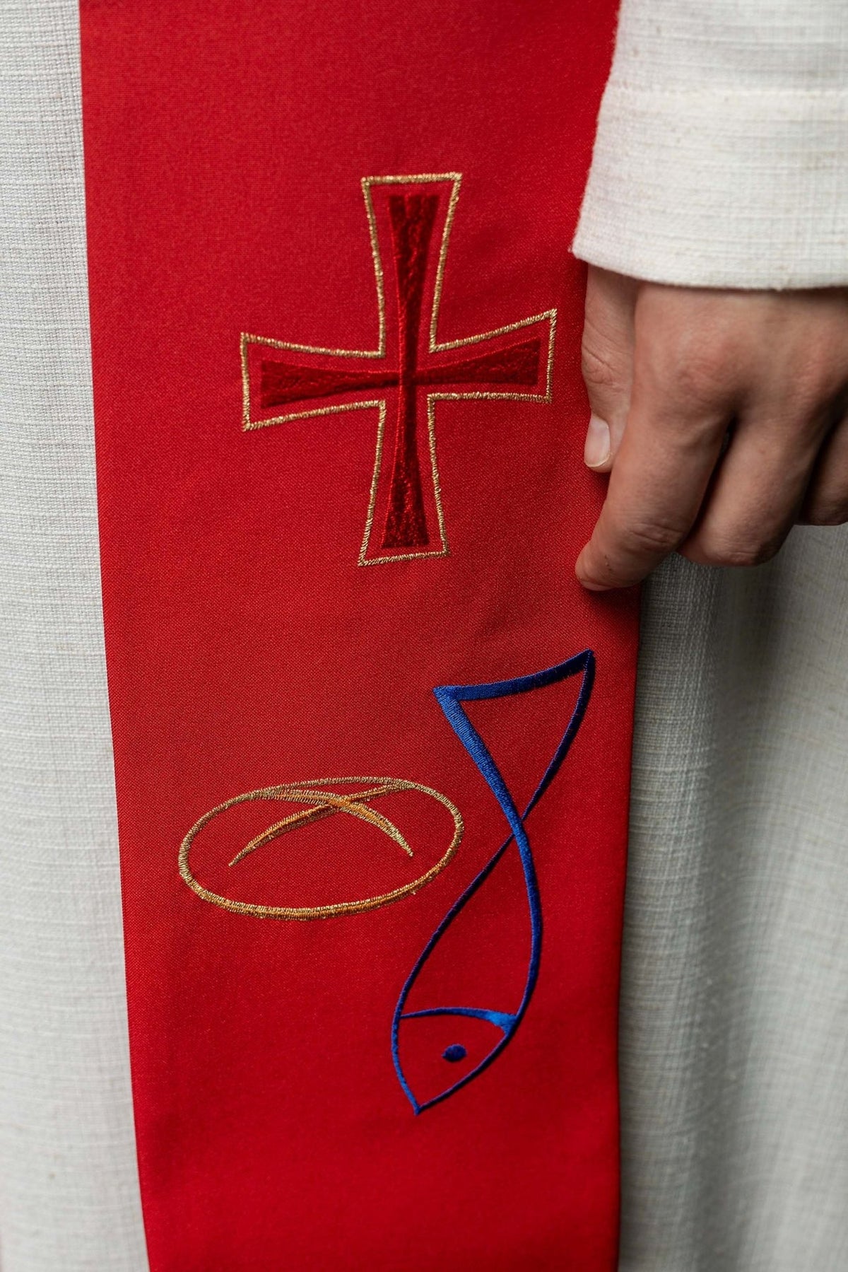 Red stole close-up showing embroidered cross, bread and blue fish
