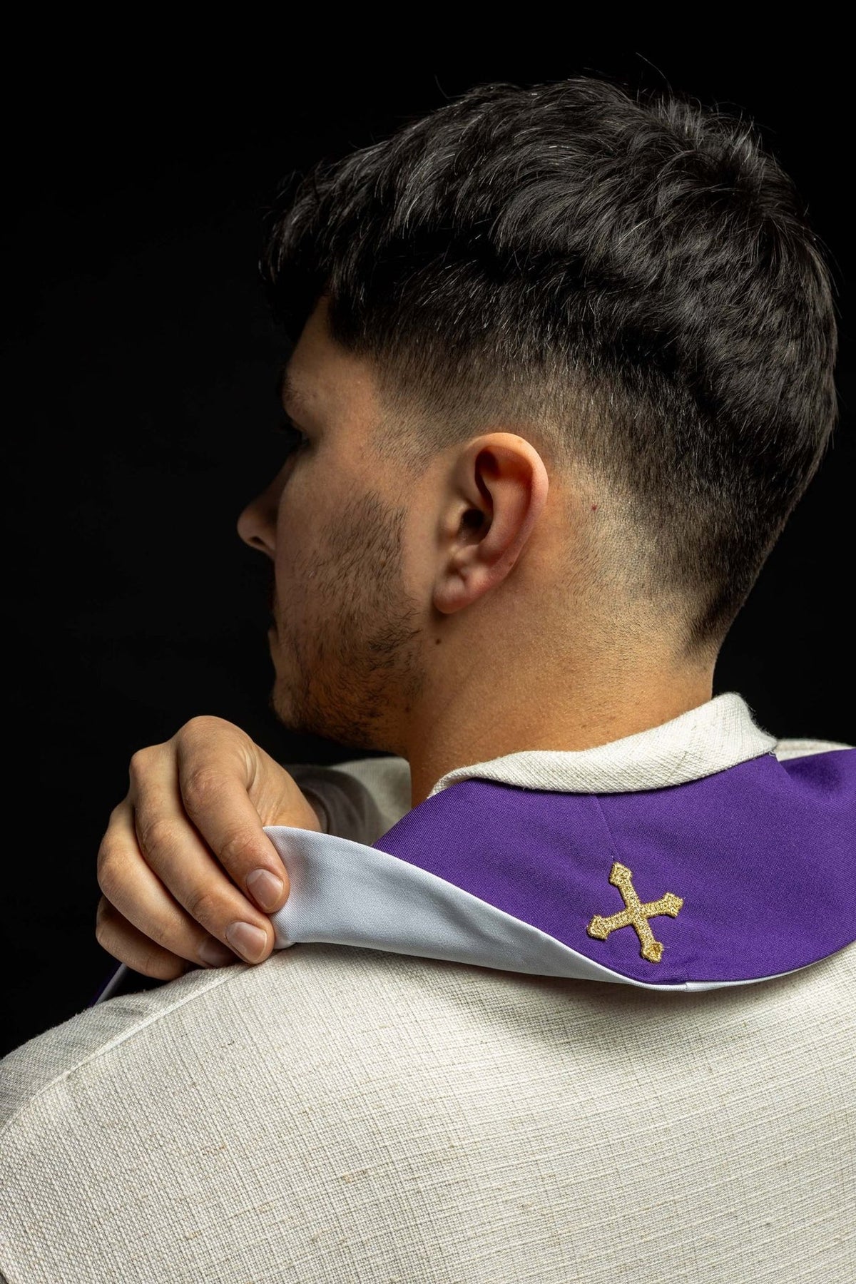 Purple and white stole worn over the shoulders, showing purple side and gold cross embroidery