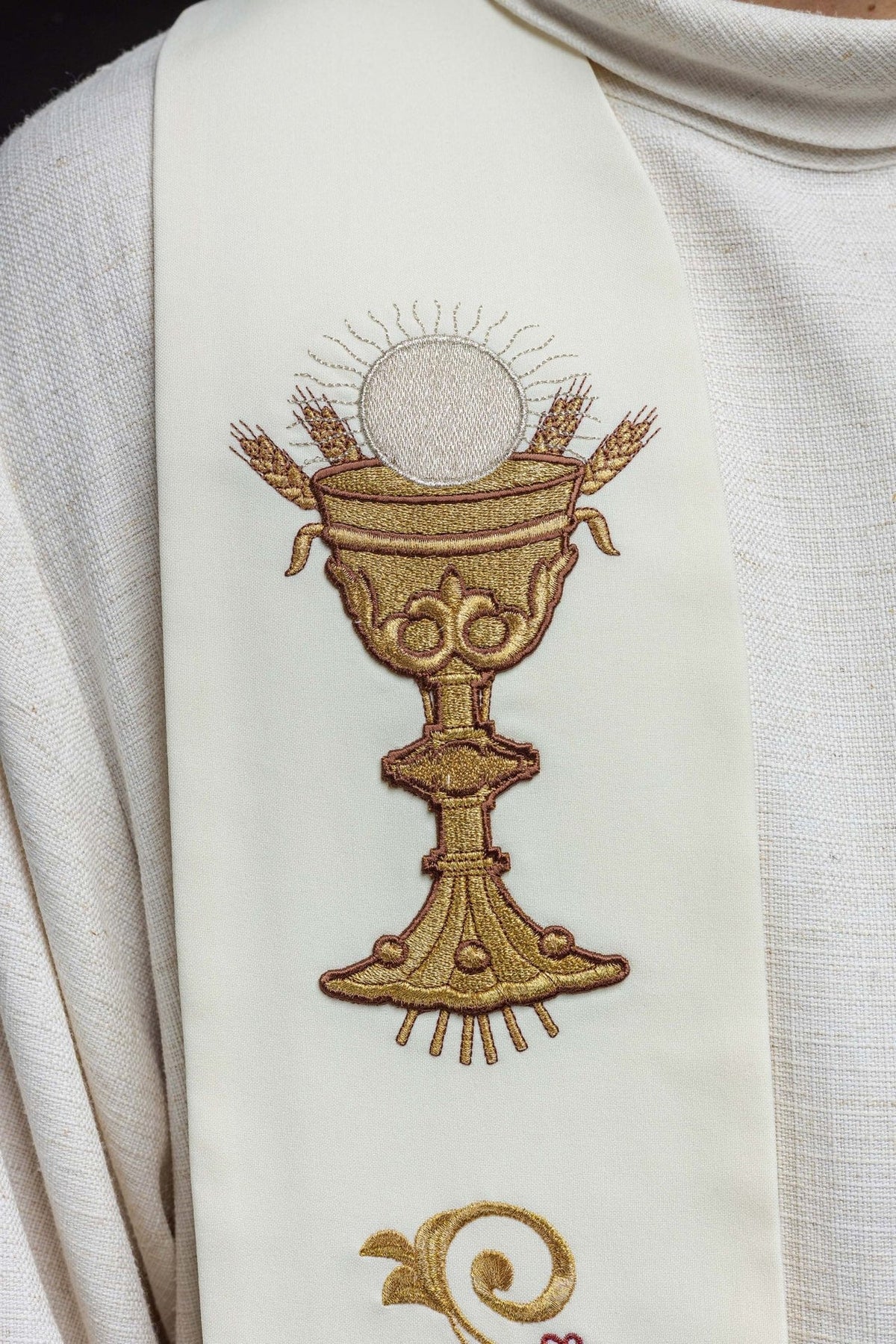 Embroidered stole close-up showing gold chalice, wheat and radiant host motif