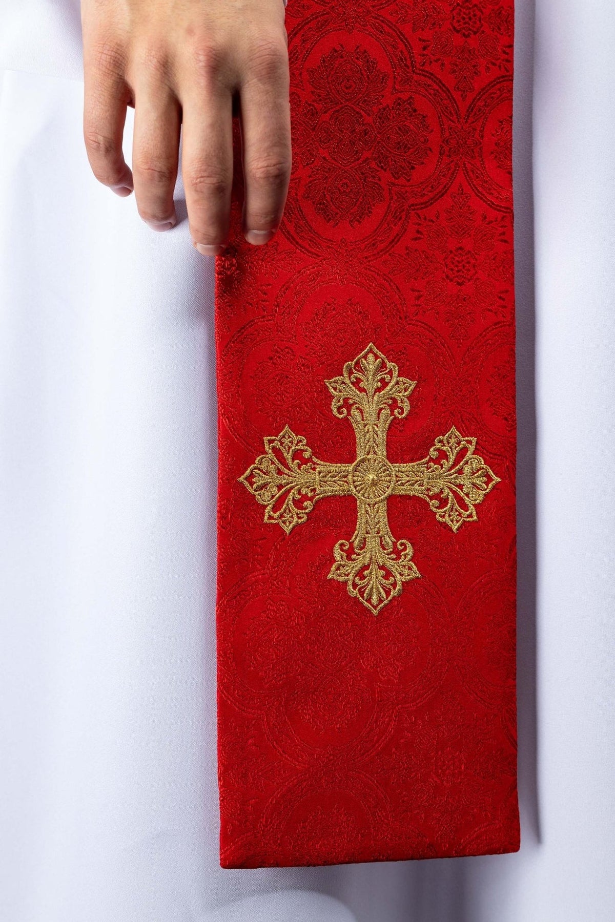 Red embroidered stole close-up with gold cross on jacquard fabric
