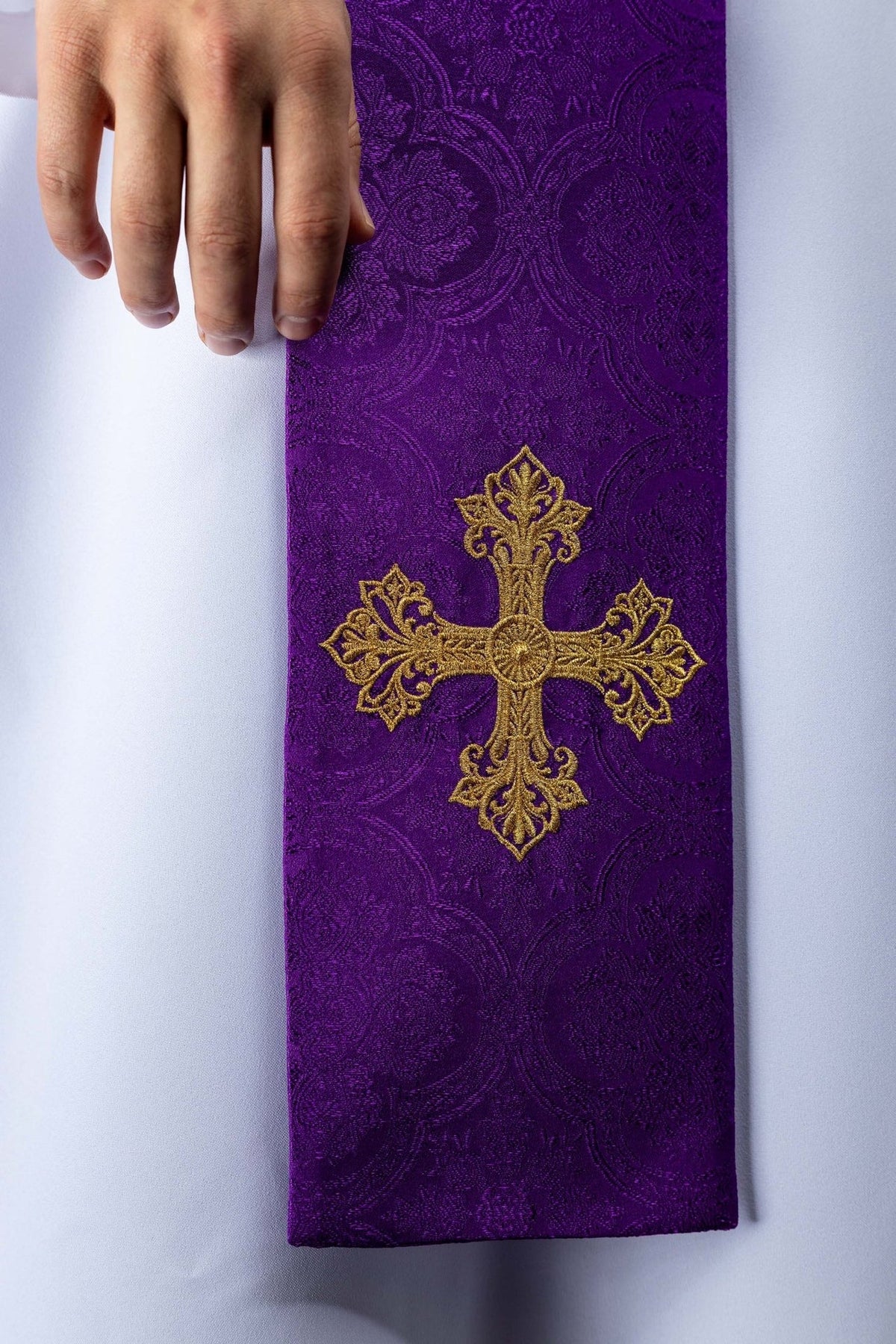 Purple stole close-up showing embroidered gold cross on floral jacquard fabric
