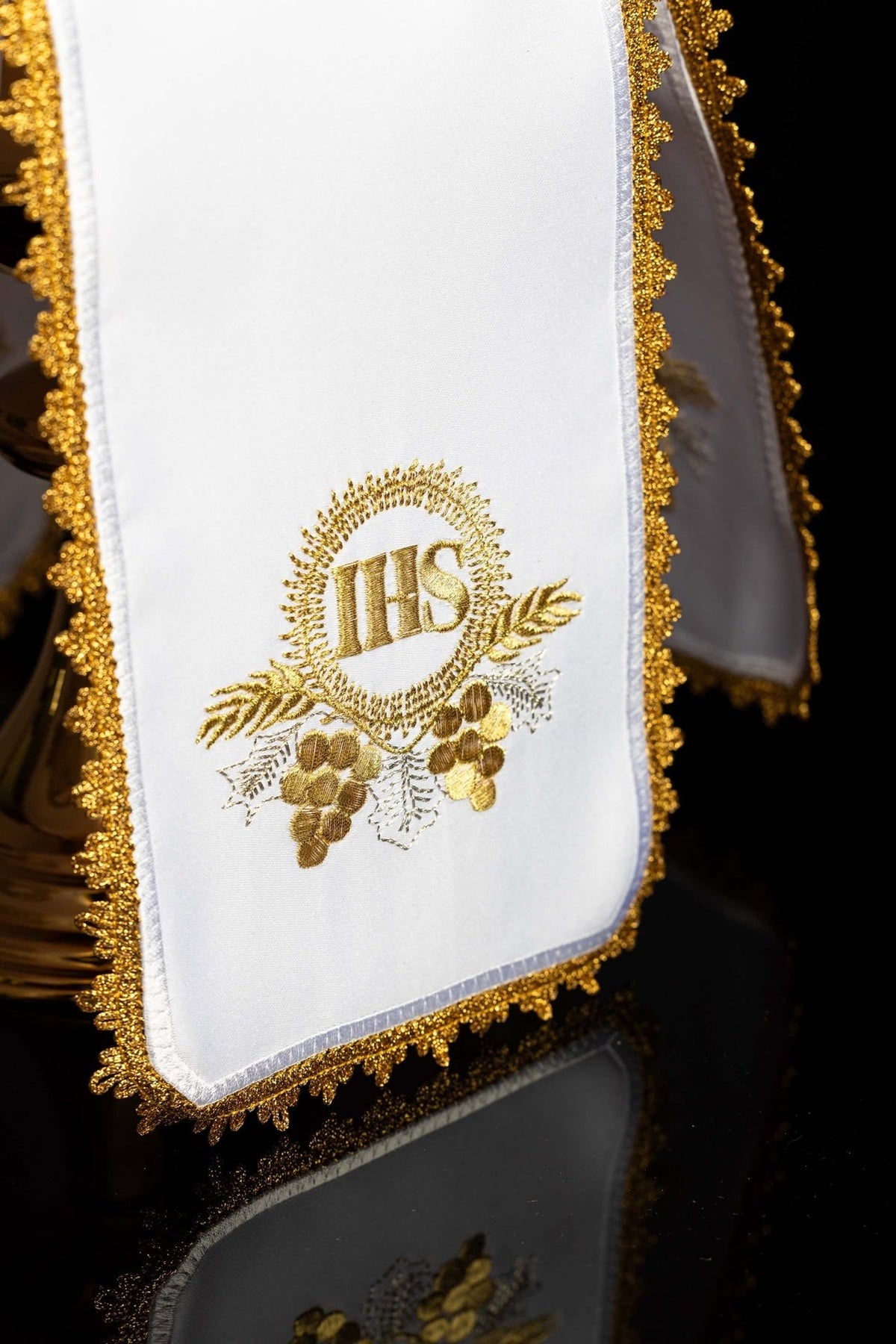 Ciborium veil close-up showing white fabric and gold IHS monogram embroidery with grapes and wheat