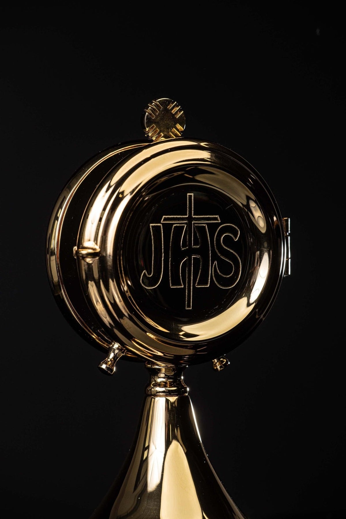 Brass luna holder close-up showing the raised IHS monogram and cross on its front