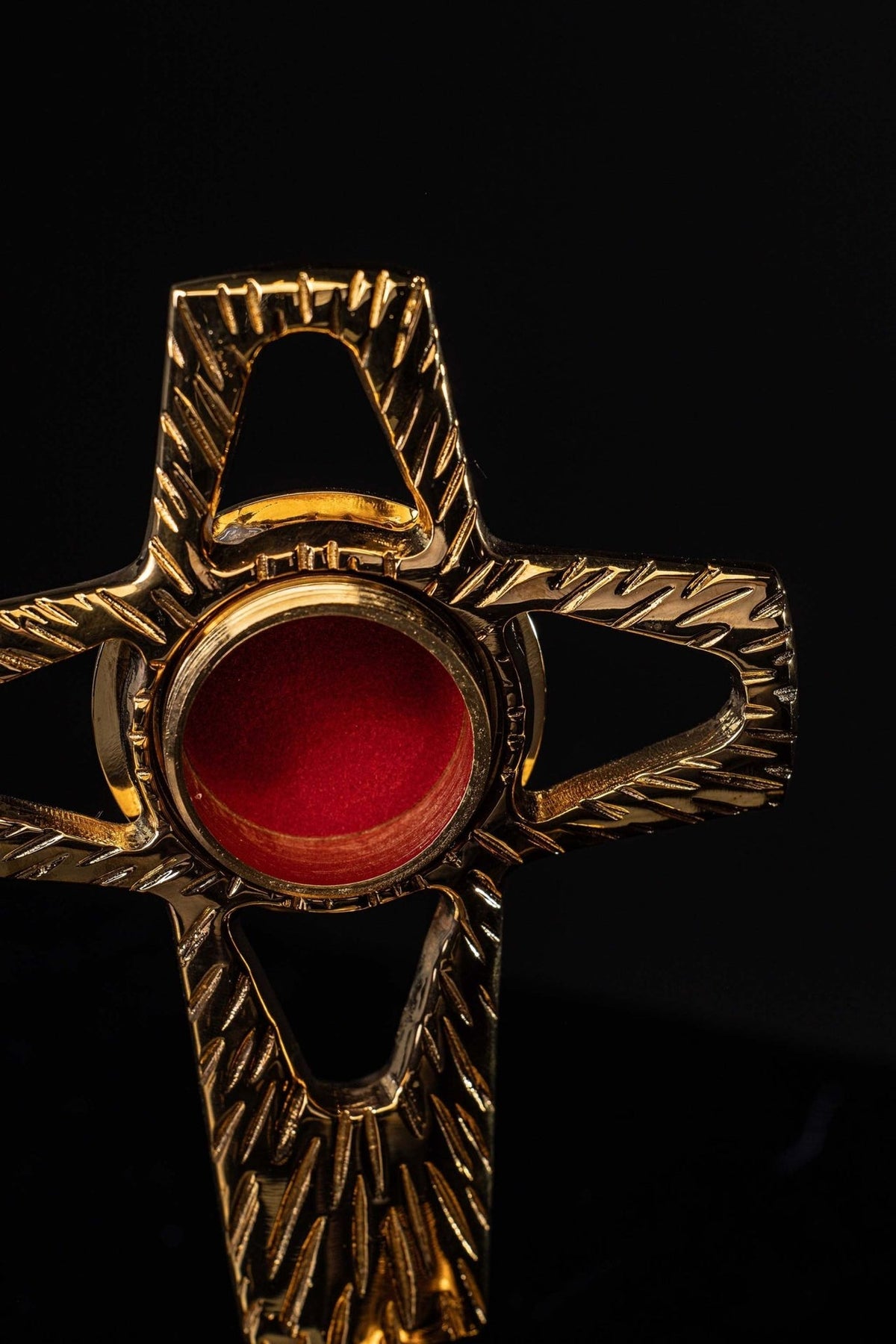 Gilded brass reliquary close-up with red center, circular rim and textured cross arms