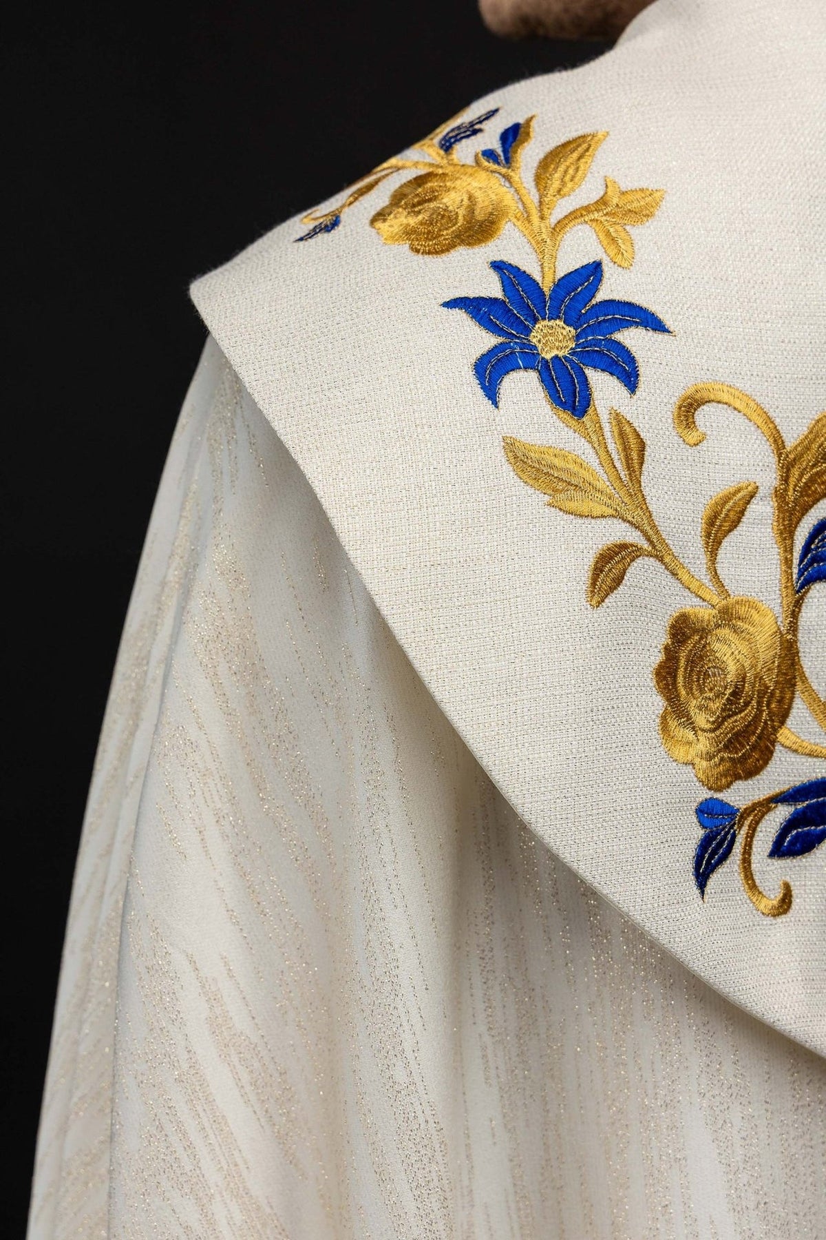 Ecru cope shoulder close-up with blue flower and gold embroidered trim