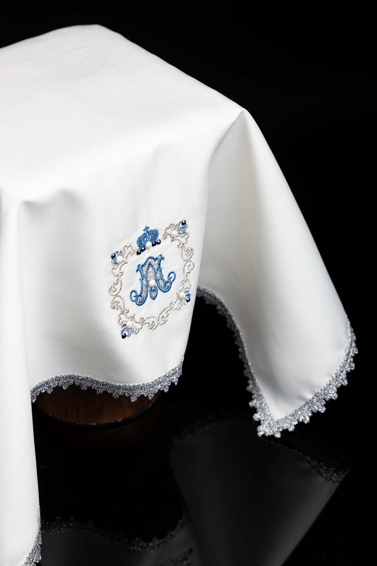 Ecru chalice veil angled view with blue Marian symbol and ornate silver edging