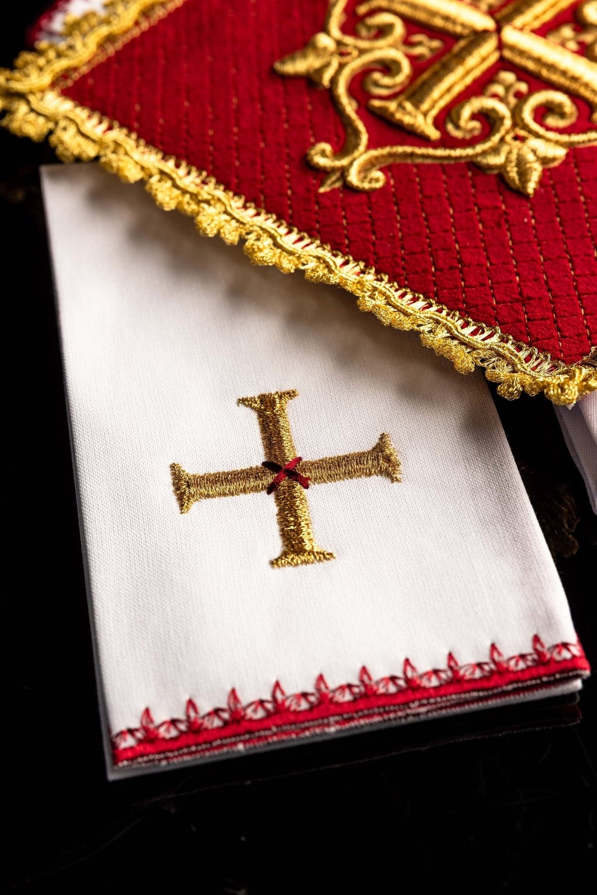 White altar linen close-up with gold embroidered cross and red decorative border