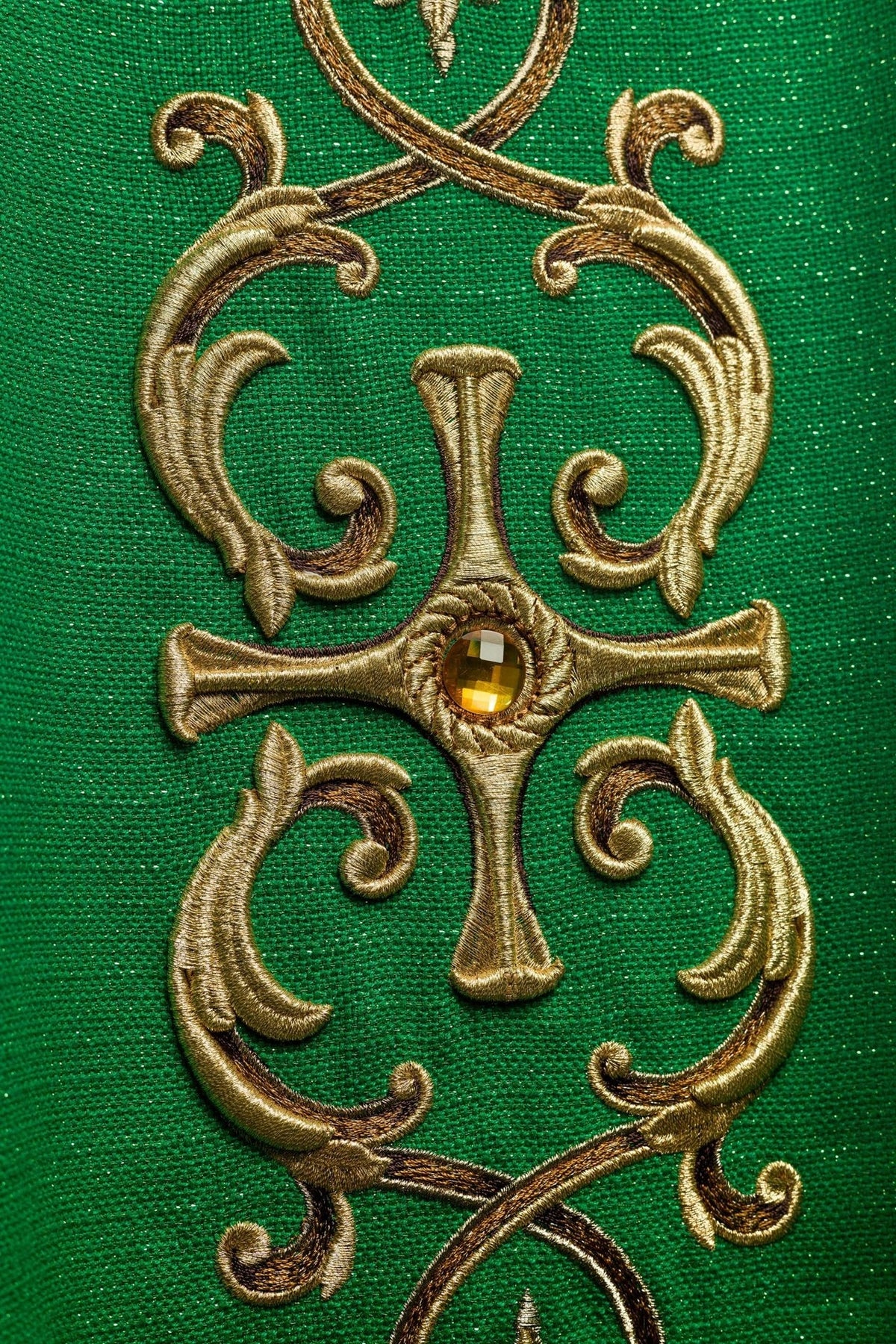 Green chasuble close-up showing gold cross embroidery with stone