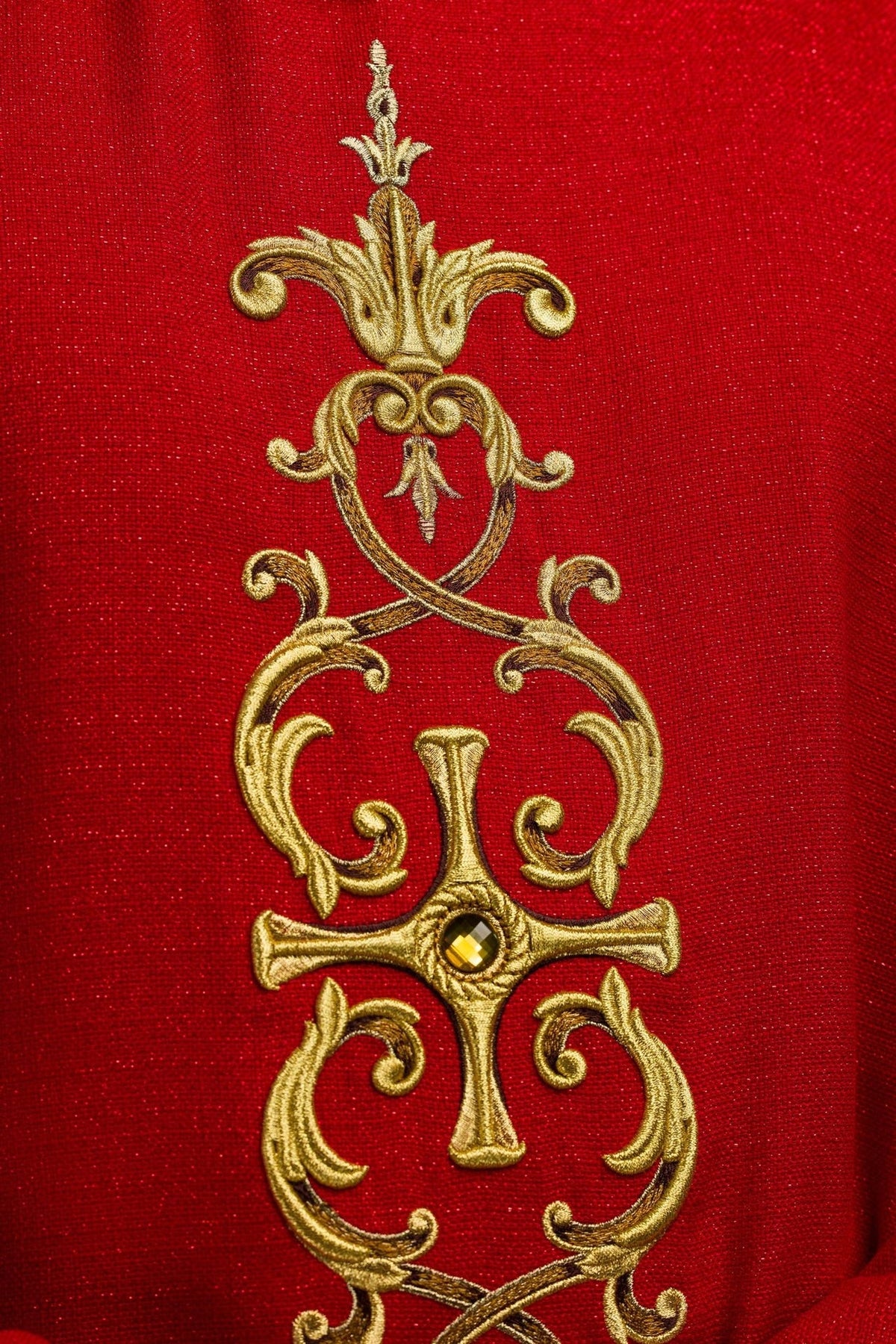 Red chasuble close-up showing ornate gold embroidery and a central stone