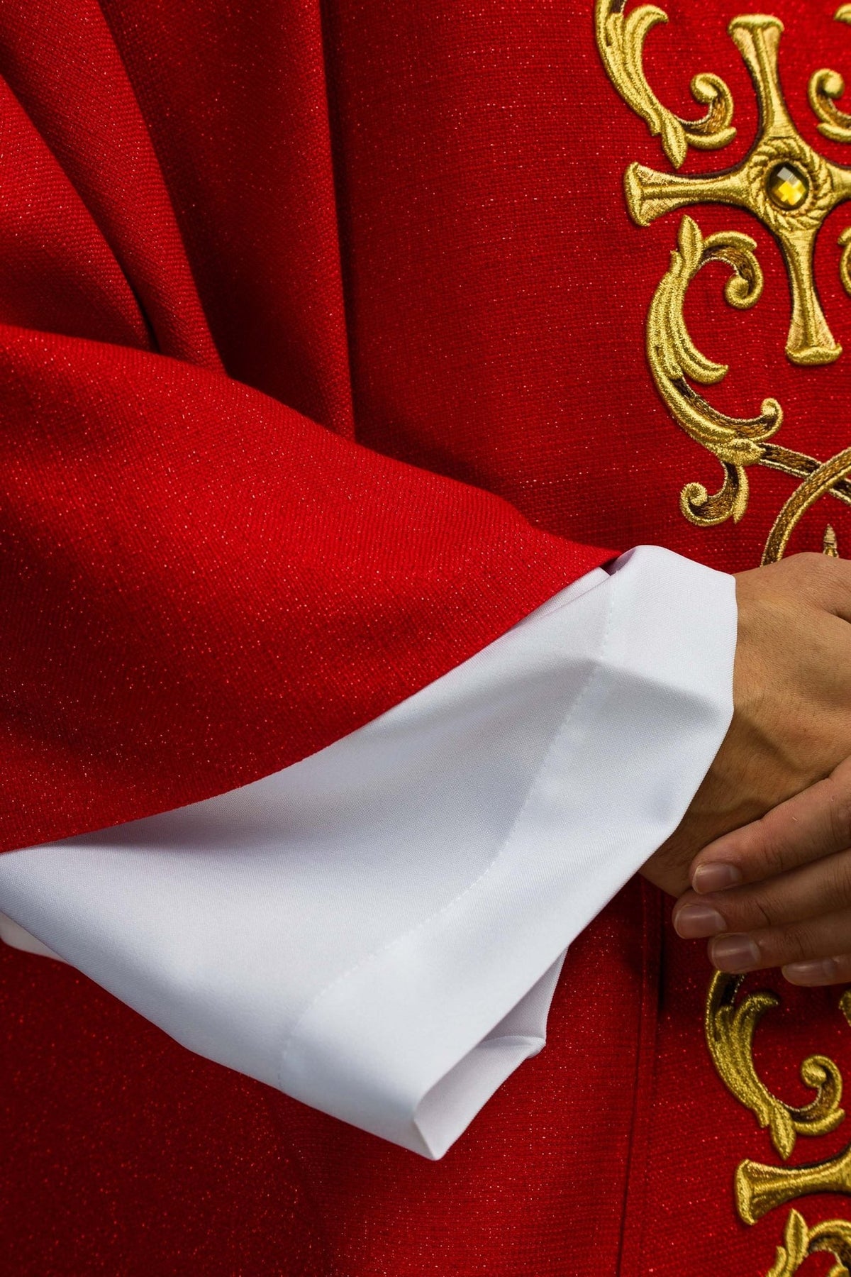 Red chasuble detail showing textured fabric, gold embroidery and sleeve edge