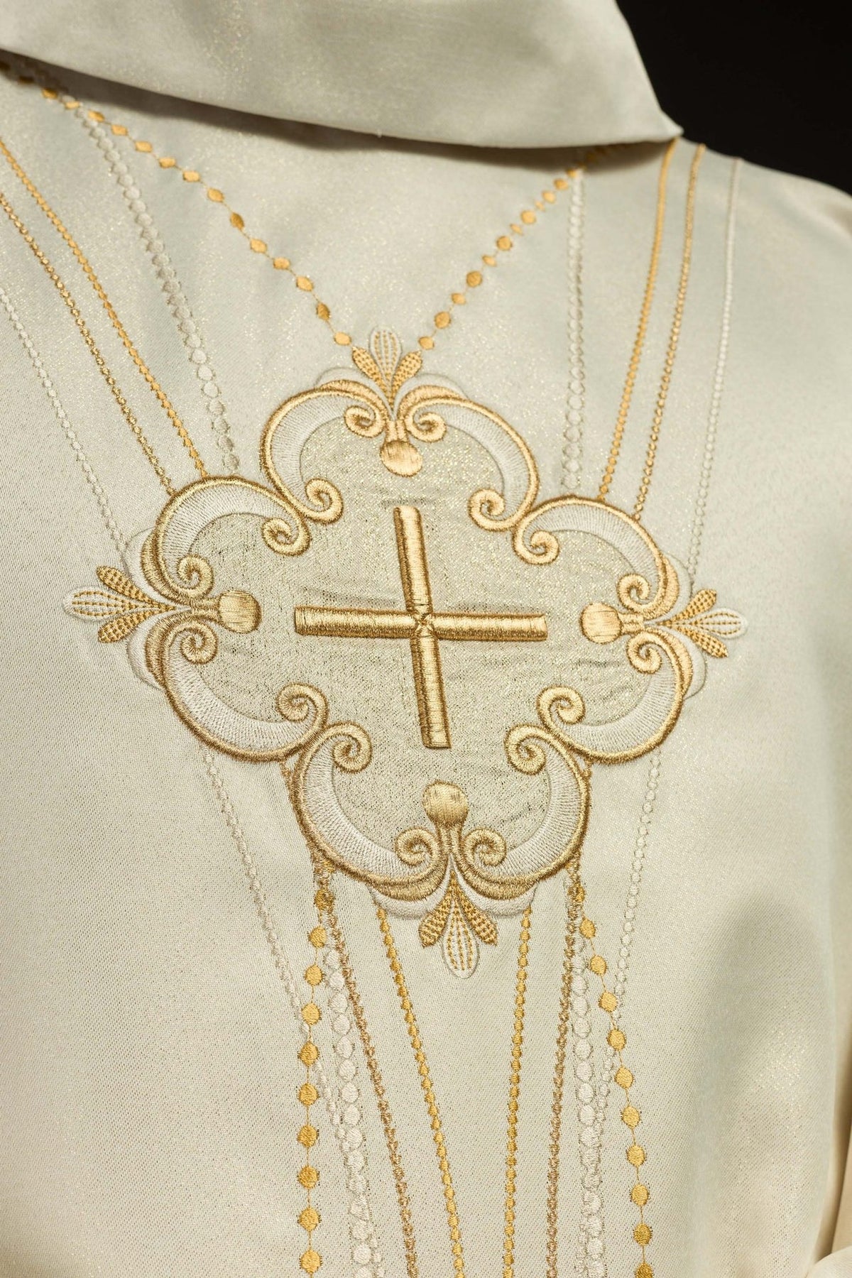 Ecru chasuble detail of ornate gold cross embroidery and rosary-inspired bead lines