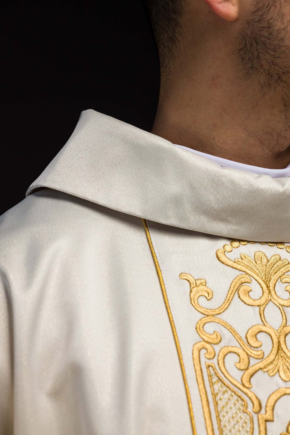 White chasuble close-up showing lustrous fabric, gold stand-up collar and embroidered orphrey