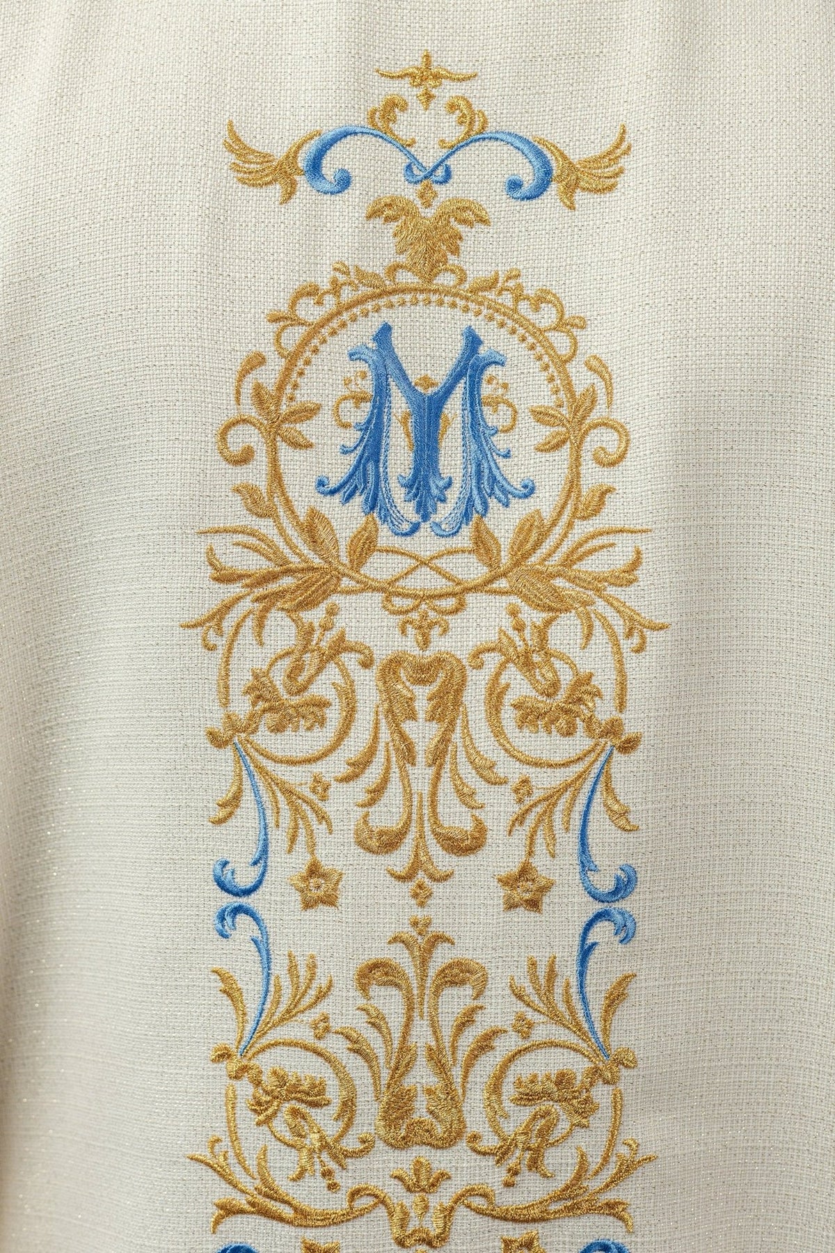 Ivory chasuble embroidered detail showing blue Marian monogram and gold ornamental thread