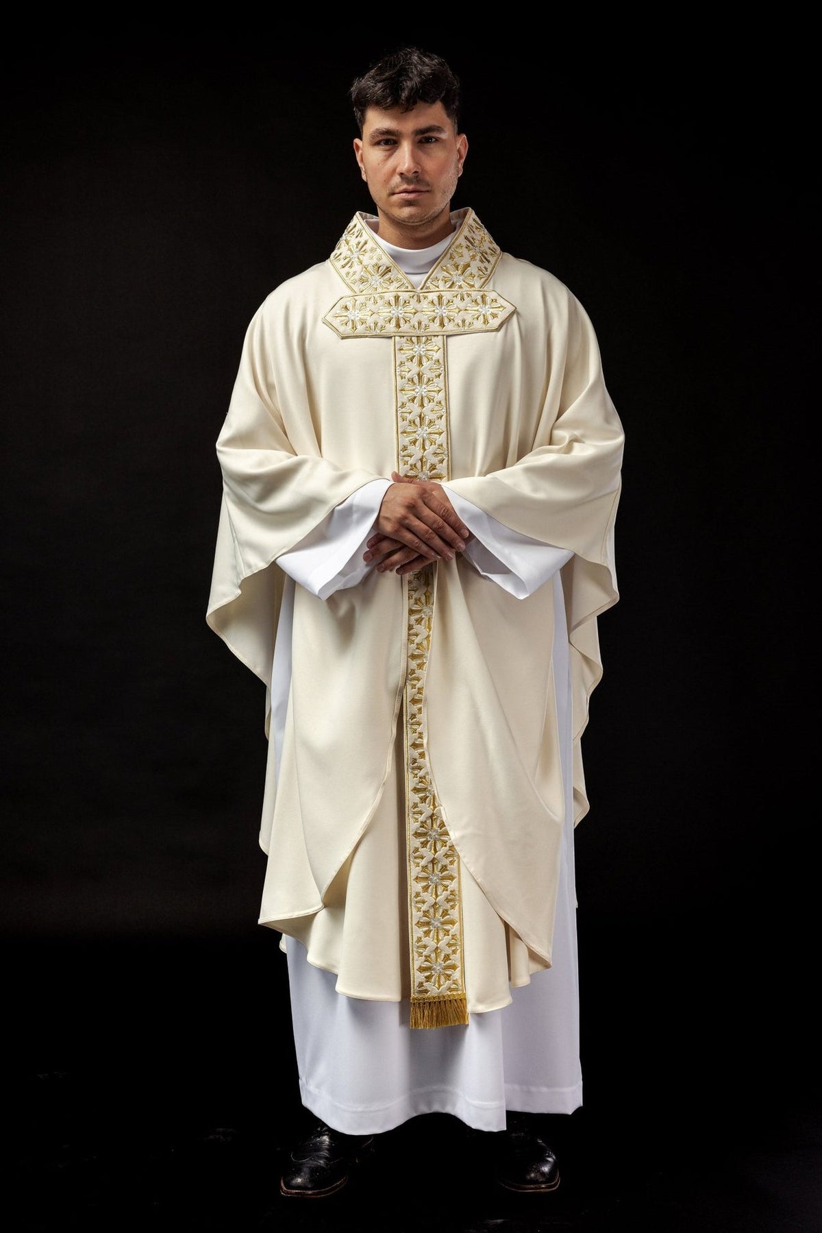 Ecru chasuble worn from the front with gold cross embroidery and flowing sleeves