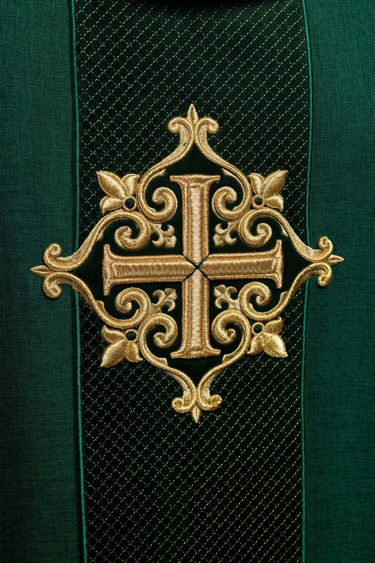 Green chasuble detail showing large gold embroidered cross on a diamond-patterned panel