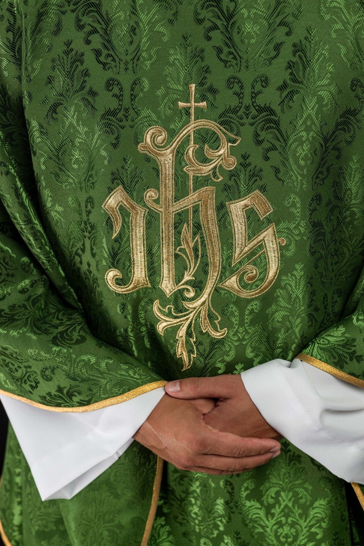 Green chasuble close-up showing embroidered gold IHS motif on decorative fabric