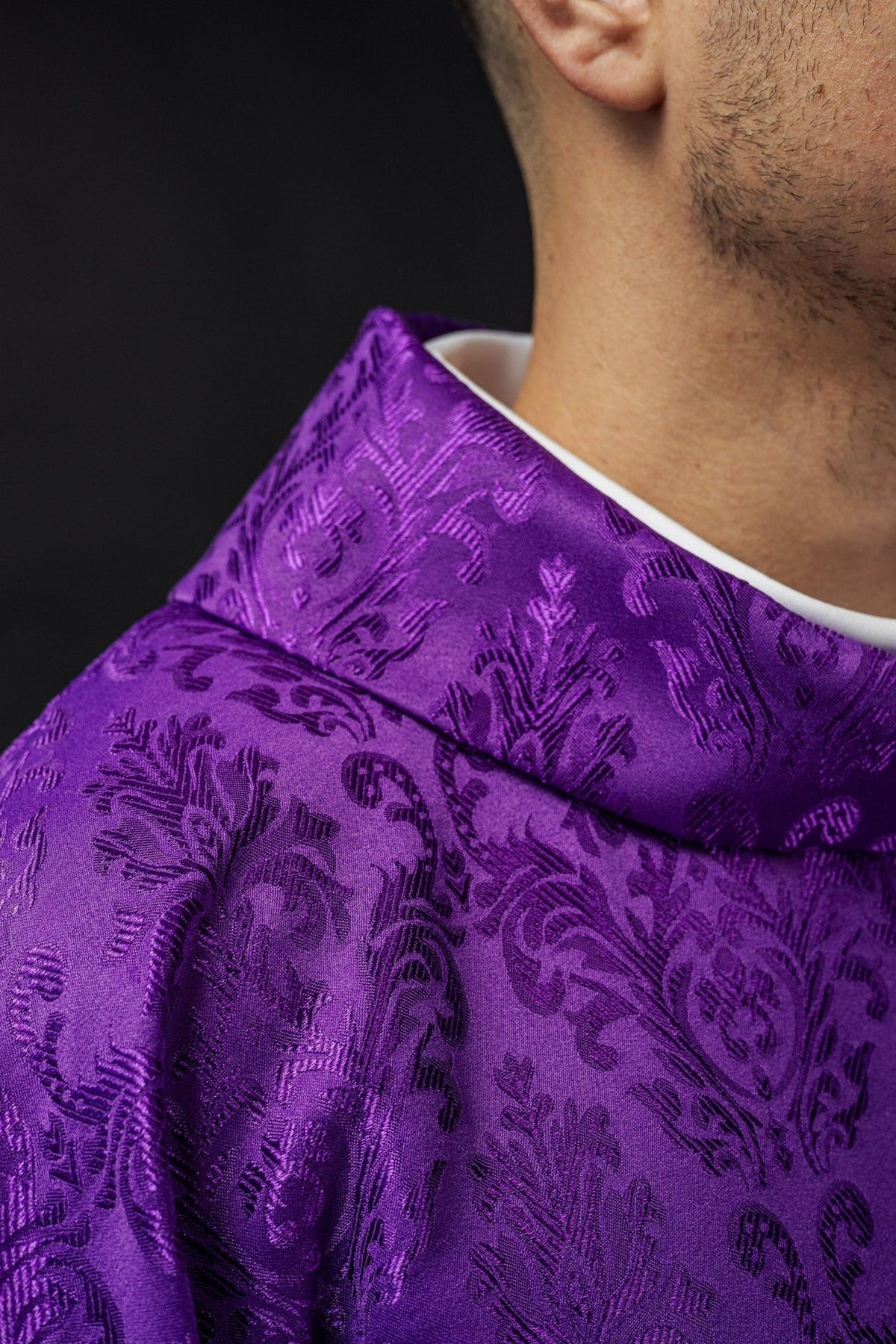 Purple chasuble close-up showing patterned fabric and gold sleeve trim