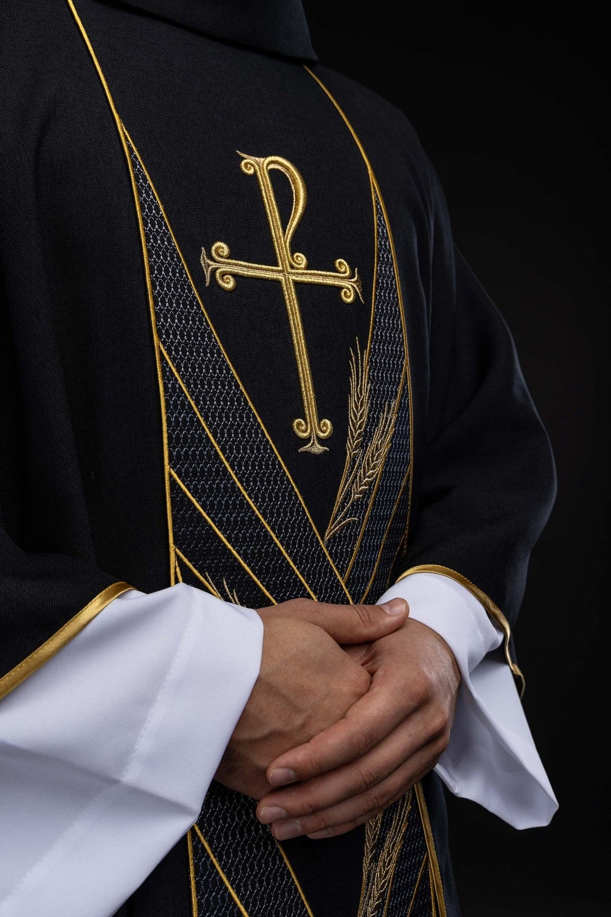 Black chasuble angled front view showing gold cross, wheat embroidery and patterned orphrey