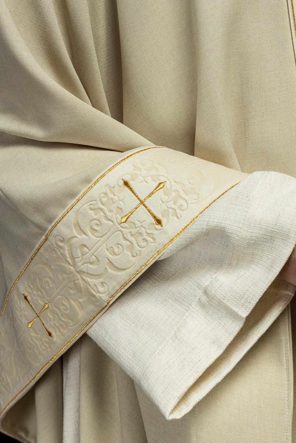 Ecru chasuble sleeve close-up with embroidered orphrey, gold cross and scrolling embroidery