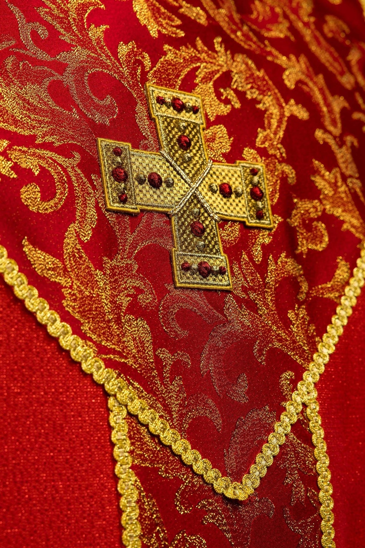 Red chasuble close-up of gold cross on floral jacquard fabric