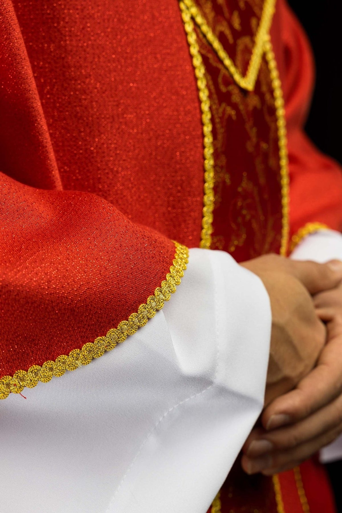 Red chasuble detail showing gold floral jacquard and braided trim