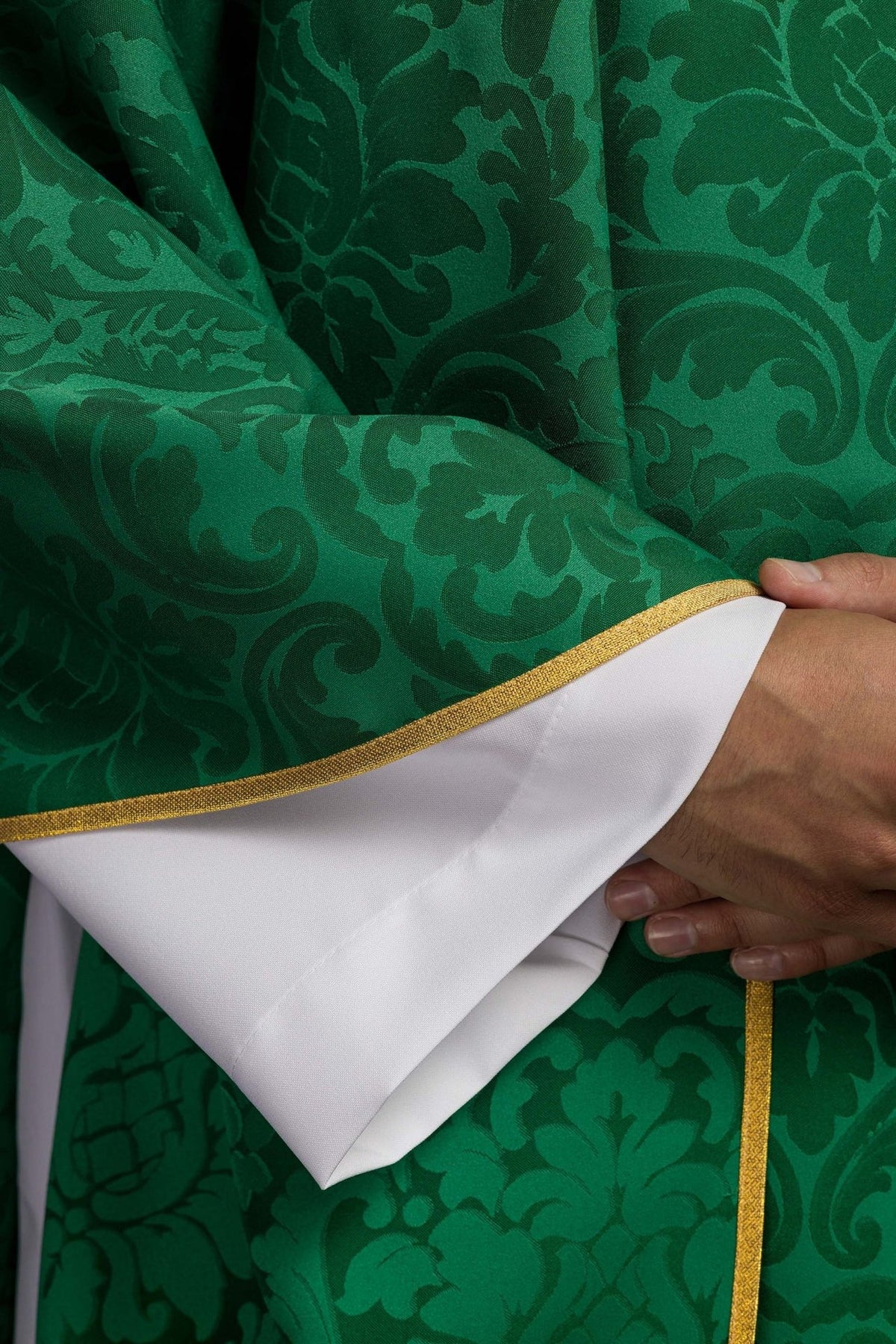 Green chasuble detail showing patterned satin, gold trim and white sleeve opening