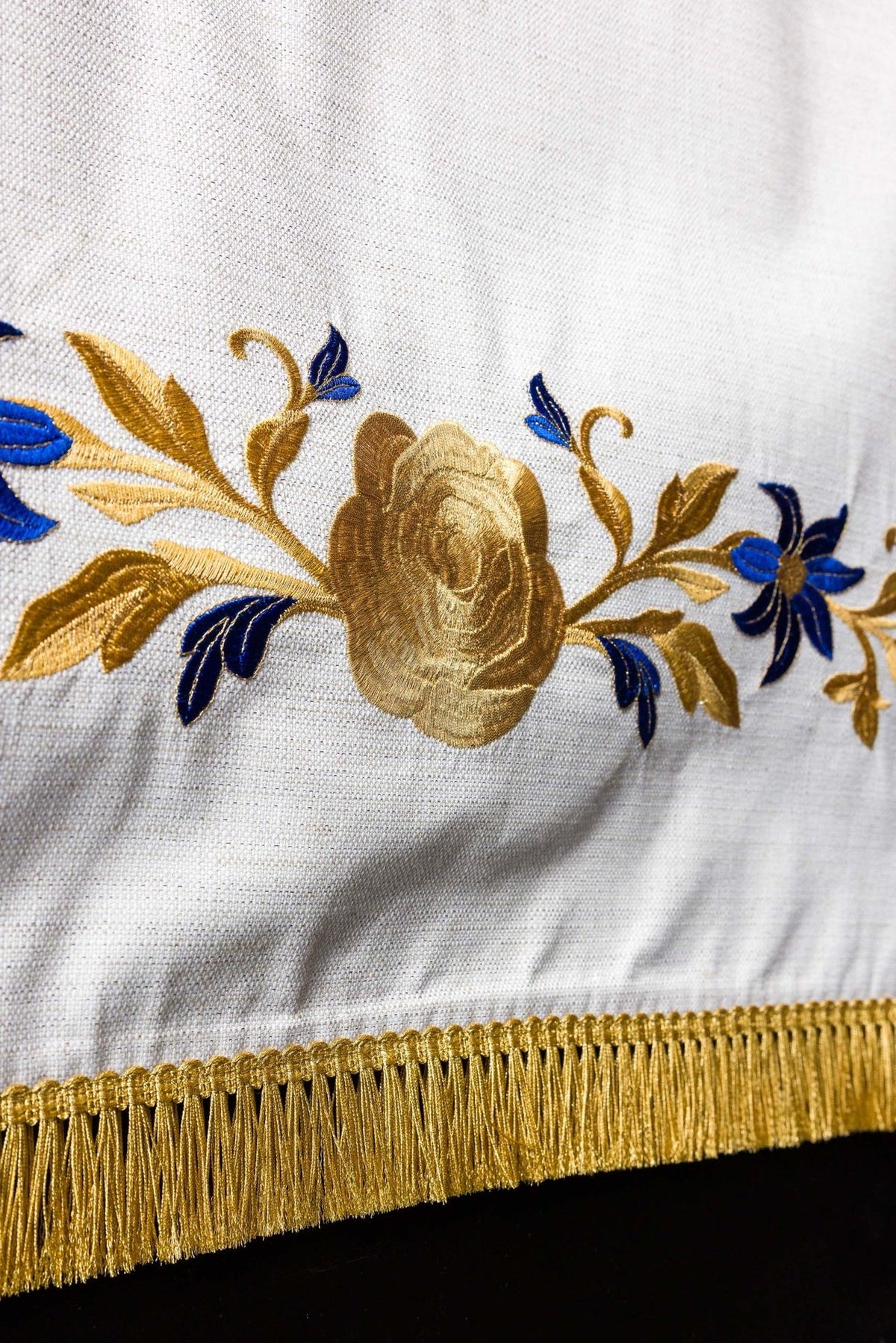 Church lectern cover detail showing embroidered gold rose, blue flowers and bottom fringe