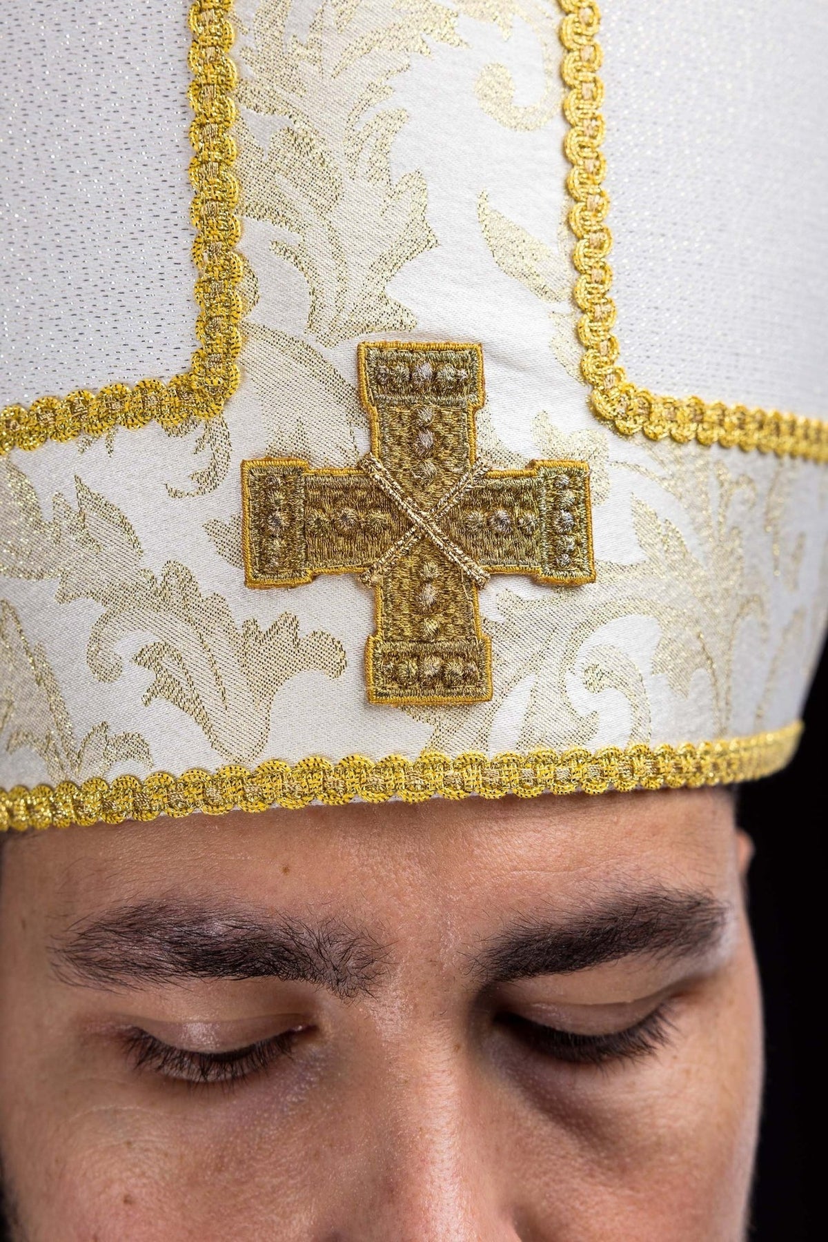 Ecru miter close-up showing embroidered gold cross and jacquard fabric