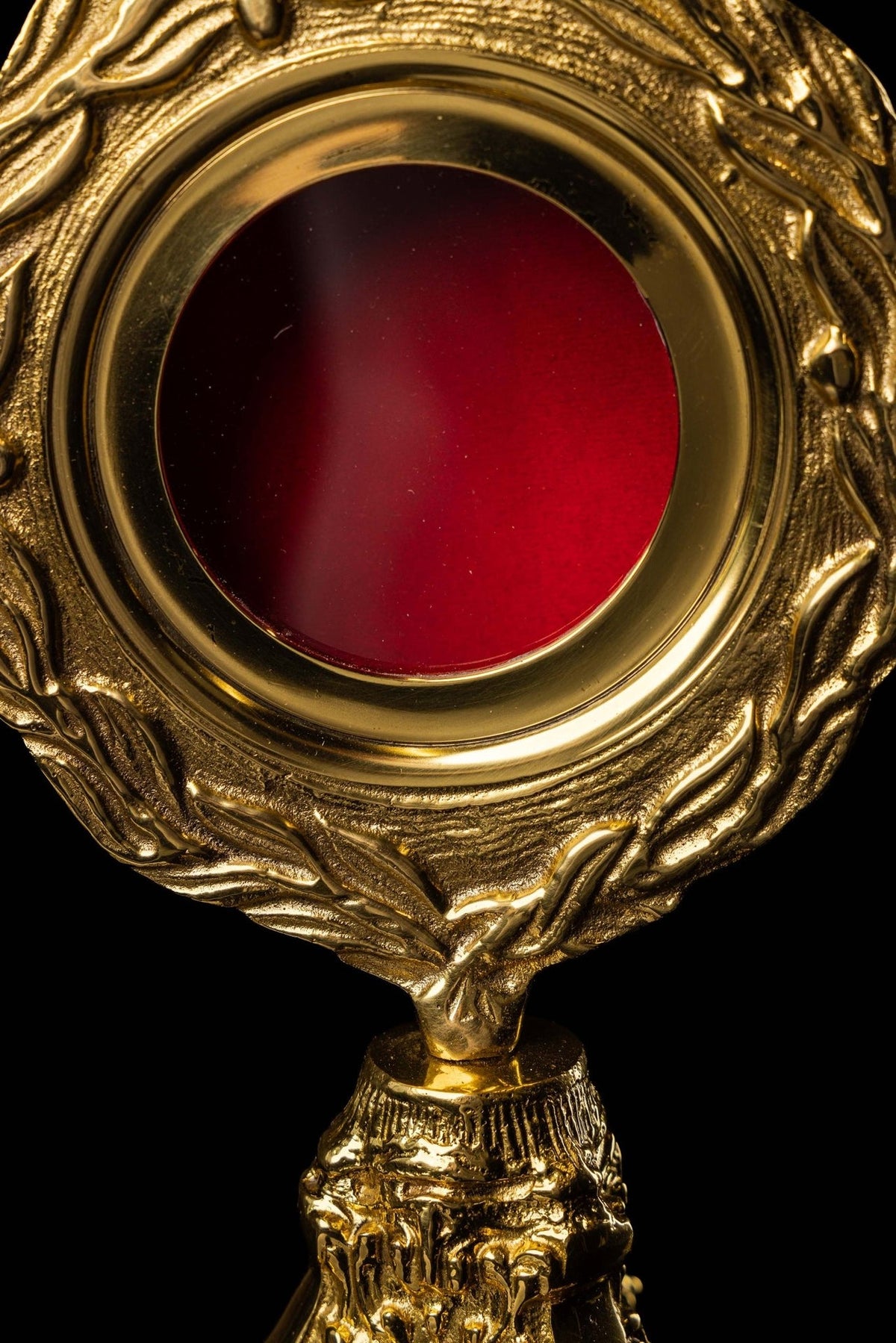 Brass reliquary close-up showing red center and raised wreath motif