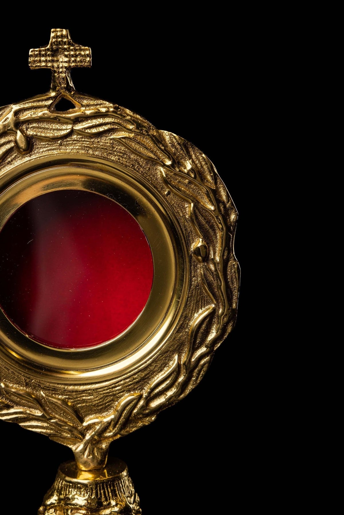 Brass reliquary angled close-up showing cross, wreath motif and red center