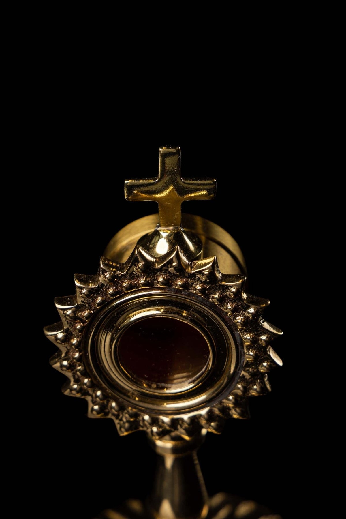 Brass reliquary upper close-up showing the cross, red center, and radiant motif