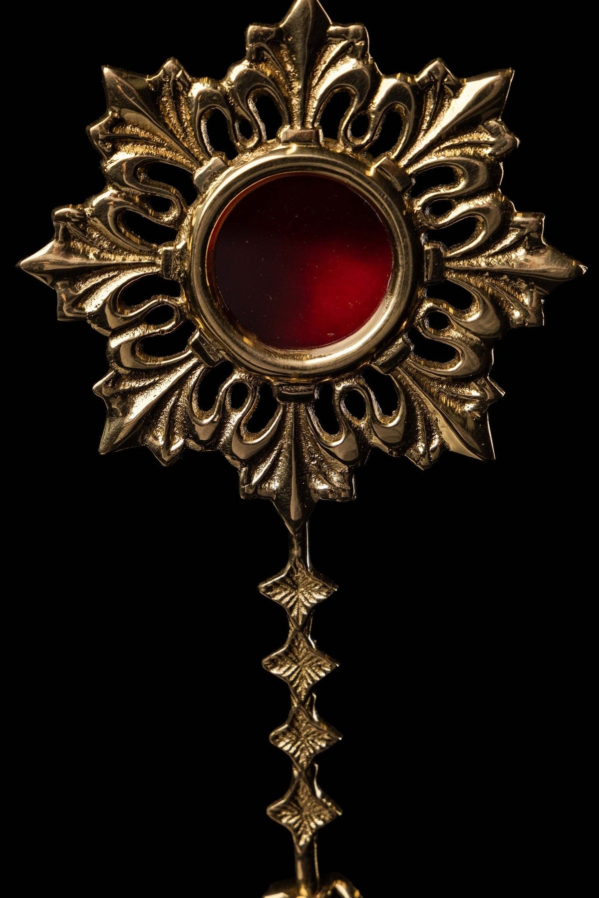Brass reliquary front close-up showing red center, raised sunburst and hanging details