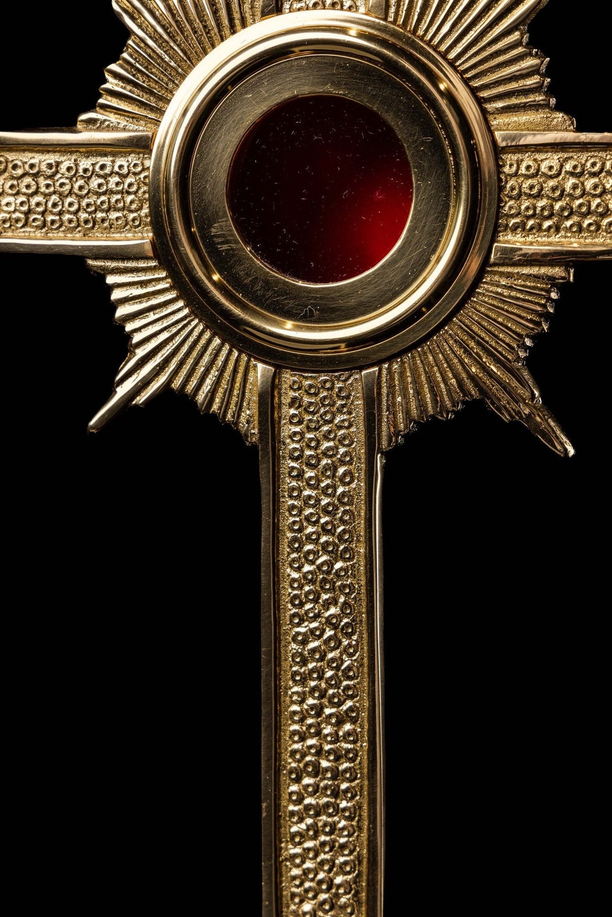 Brass cross reliquary close-up showing red center and radiant detailing