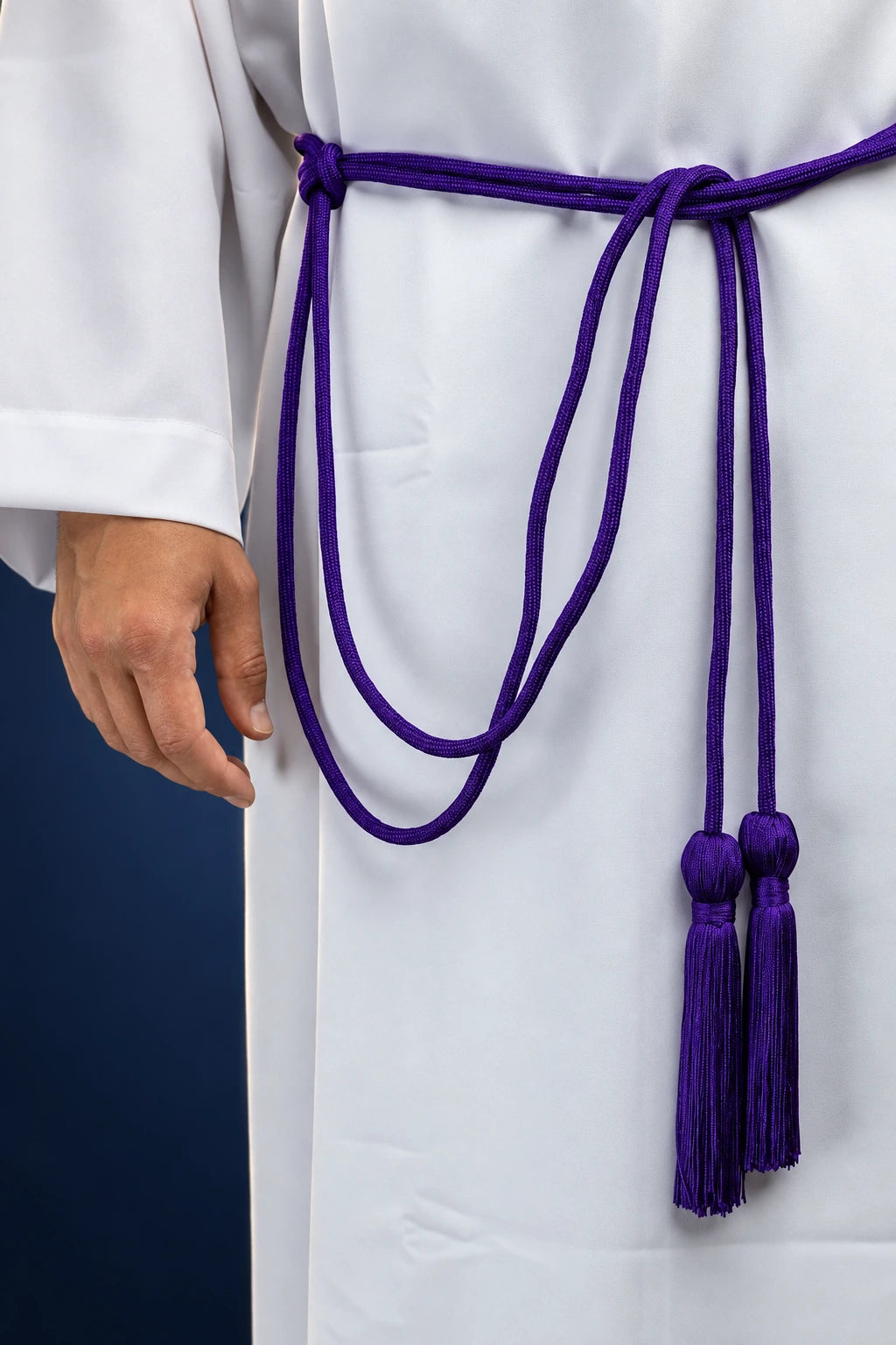 Purple cincture tied at the waist over a white alb, with two long tassels hanging front center