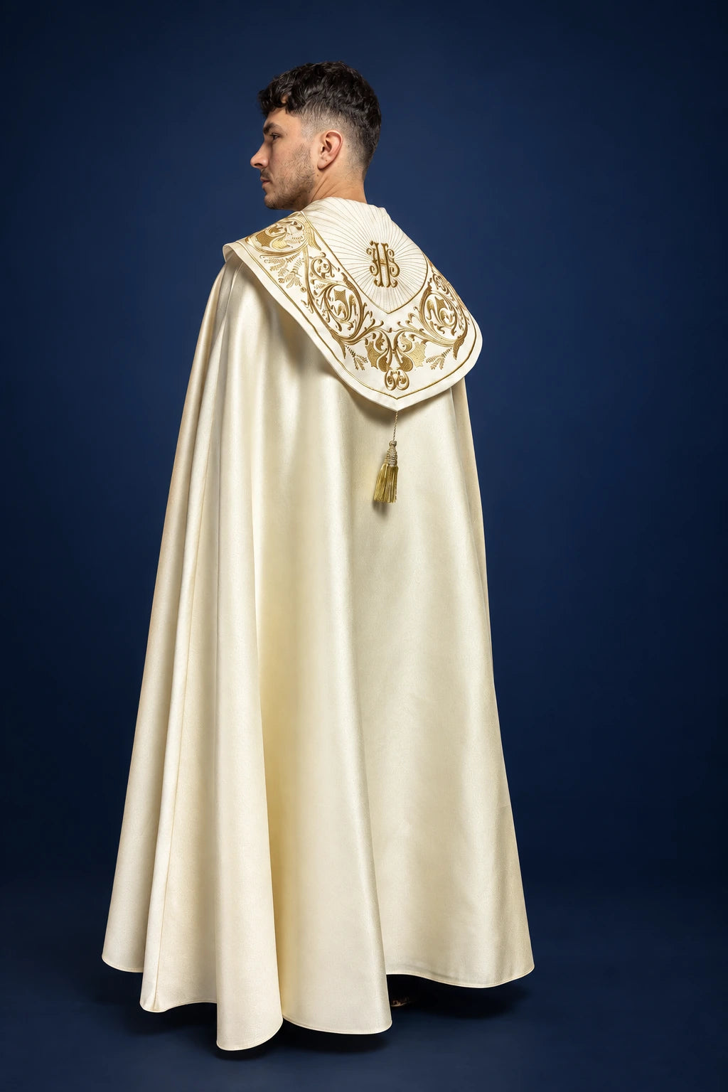 Rear three-quarter view of an ecru cope with a gold embroidered hood and long flowing hem