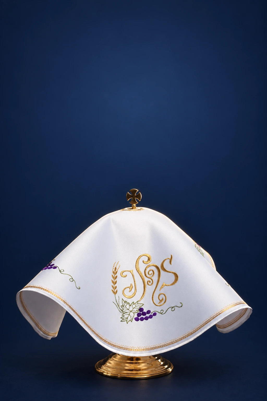 Round white ciborium veil with gold-trimmed edge and central IHS embroidery, draped over the vessel