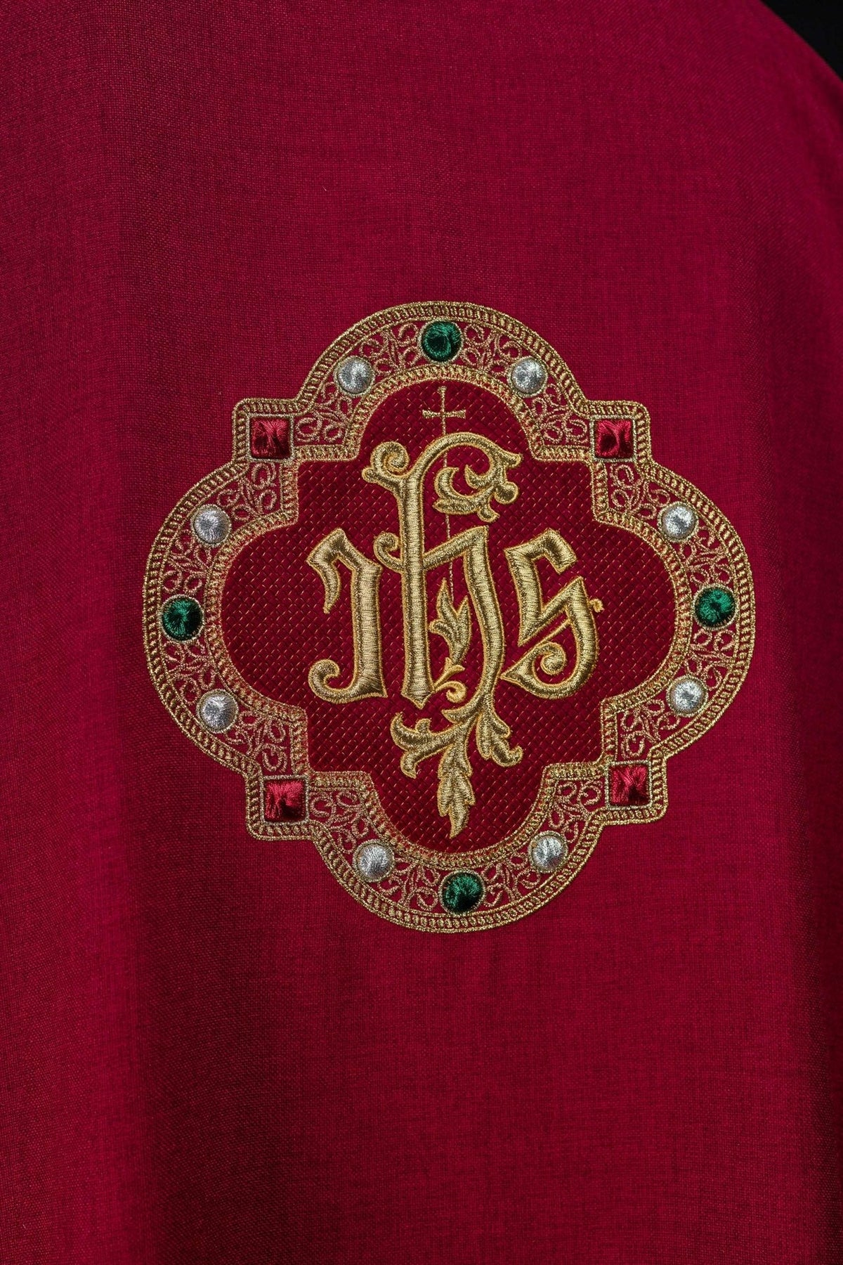 Red dalmatic close-up showing detailed embroidered IHS symbol