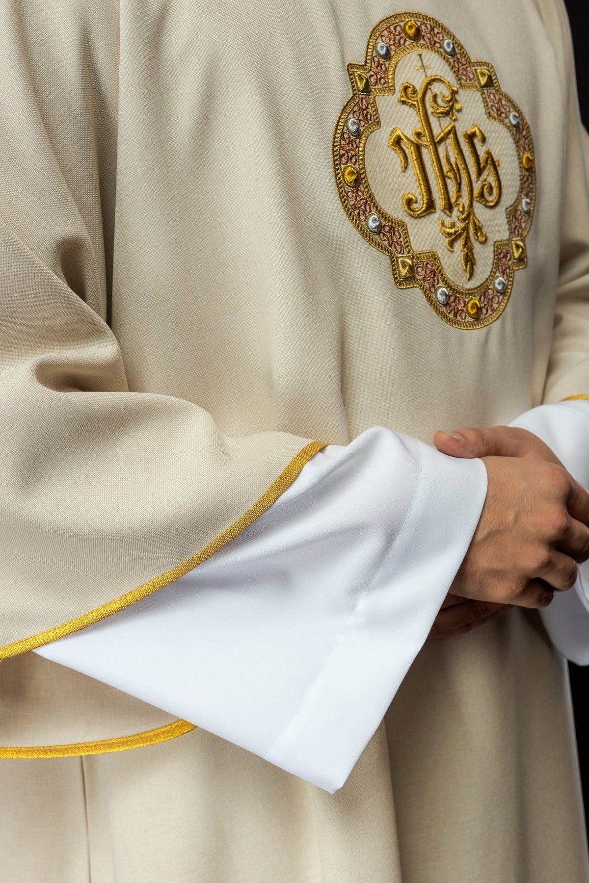 Ecru dalmatic close-up of embroidered IHS motif and gold-edged sleeve trim