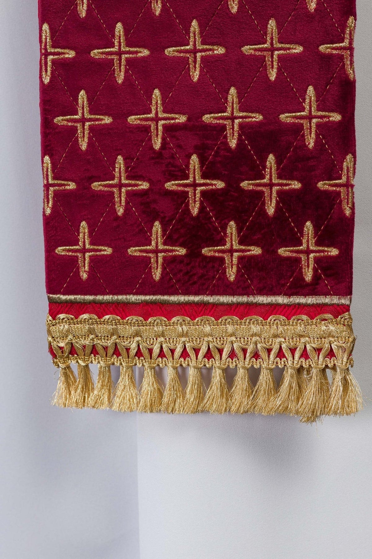 Red stole end close-up with repeated cross embroidery, gold trim and fringe
